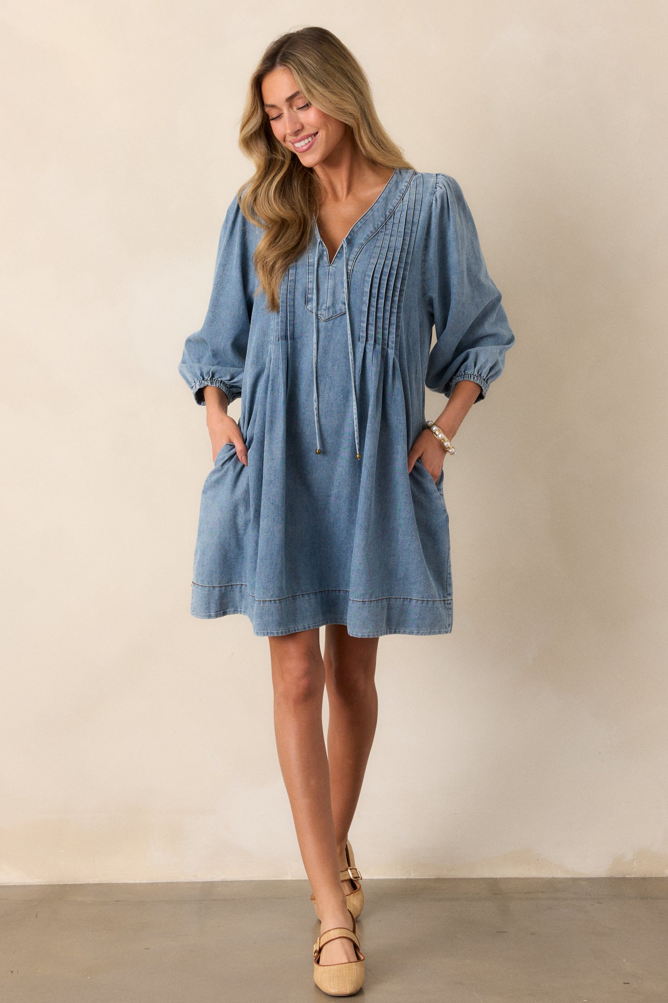 A full-body shot of the light wash denim dress, focusing on the self-tie keyhole detail and the flowy design with elastic cuffs on the sleeves.