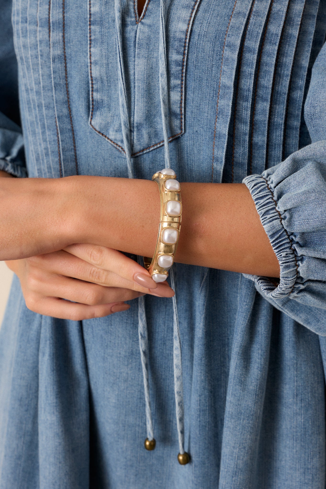 A cropped view of the gold bracelet showcasing the square ivory faux pearls arranged along the gold hardware, emphasizing the elegant design.