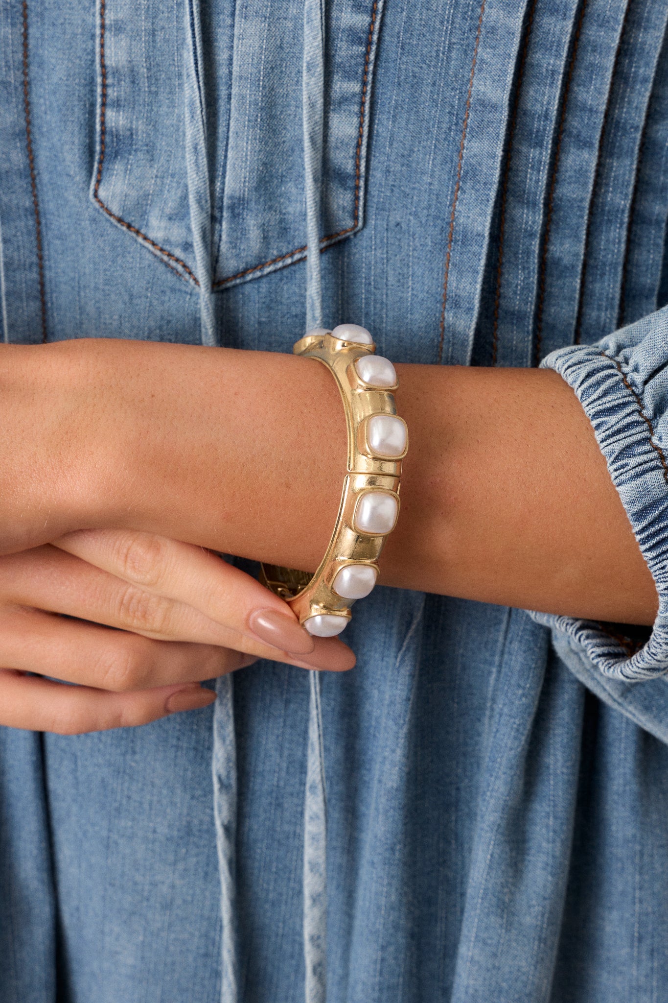 A close-up of a square ivory faux pearl on the bracelet, capturing the smooth surface and sheen against the gold hardware for a refined look.