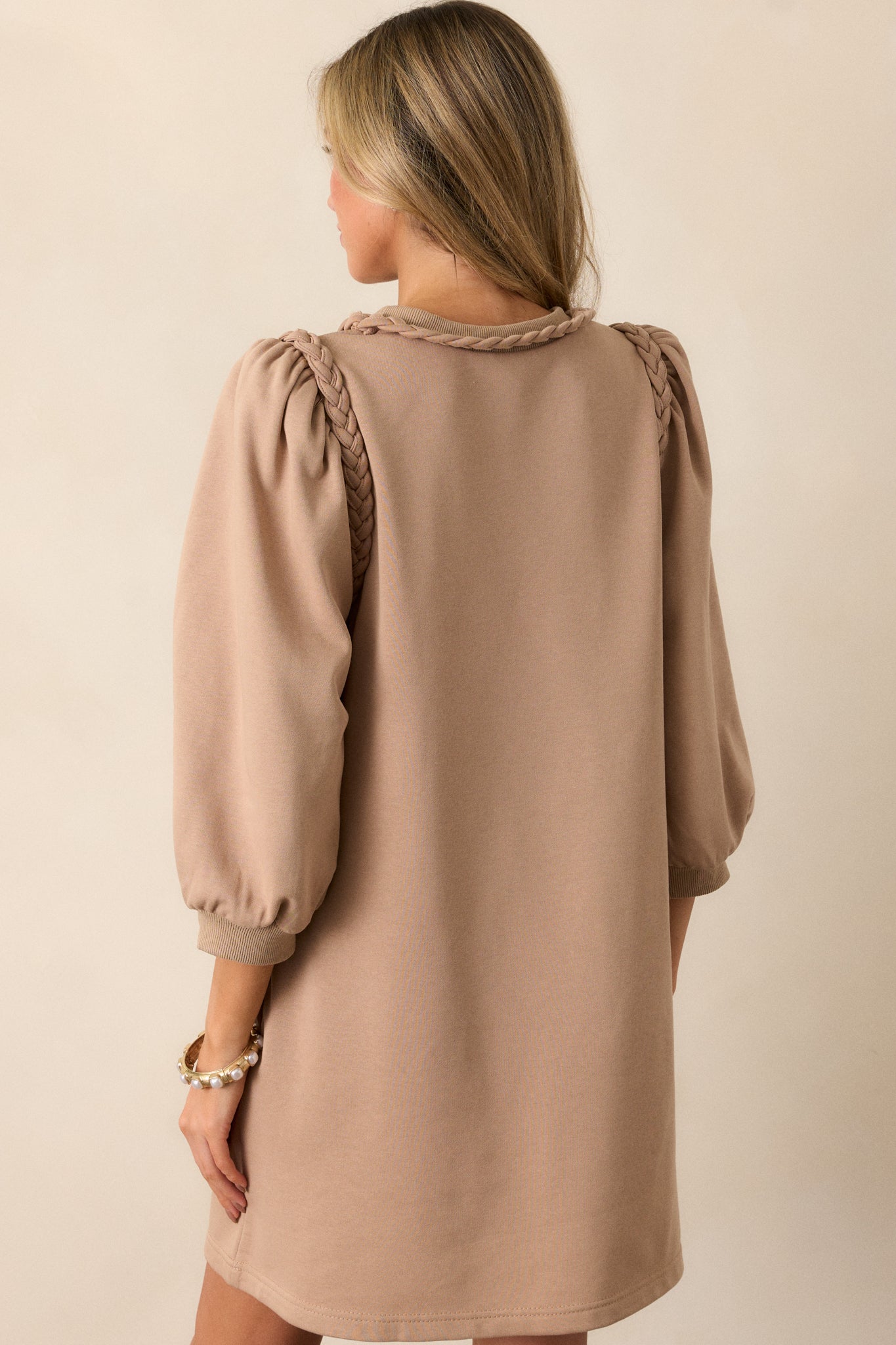 Back view of a tan dress featuring a braided neckline, braided shoulder detailing, puff 3/4 sleeves and a boxy fit.