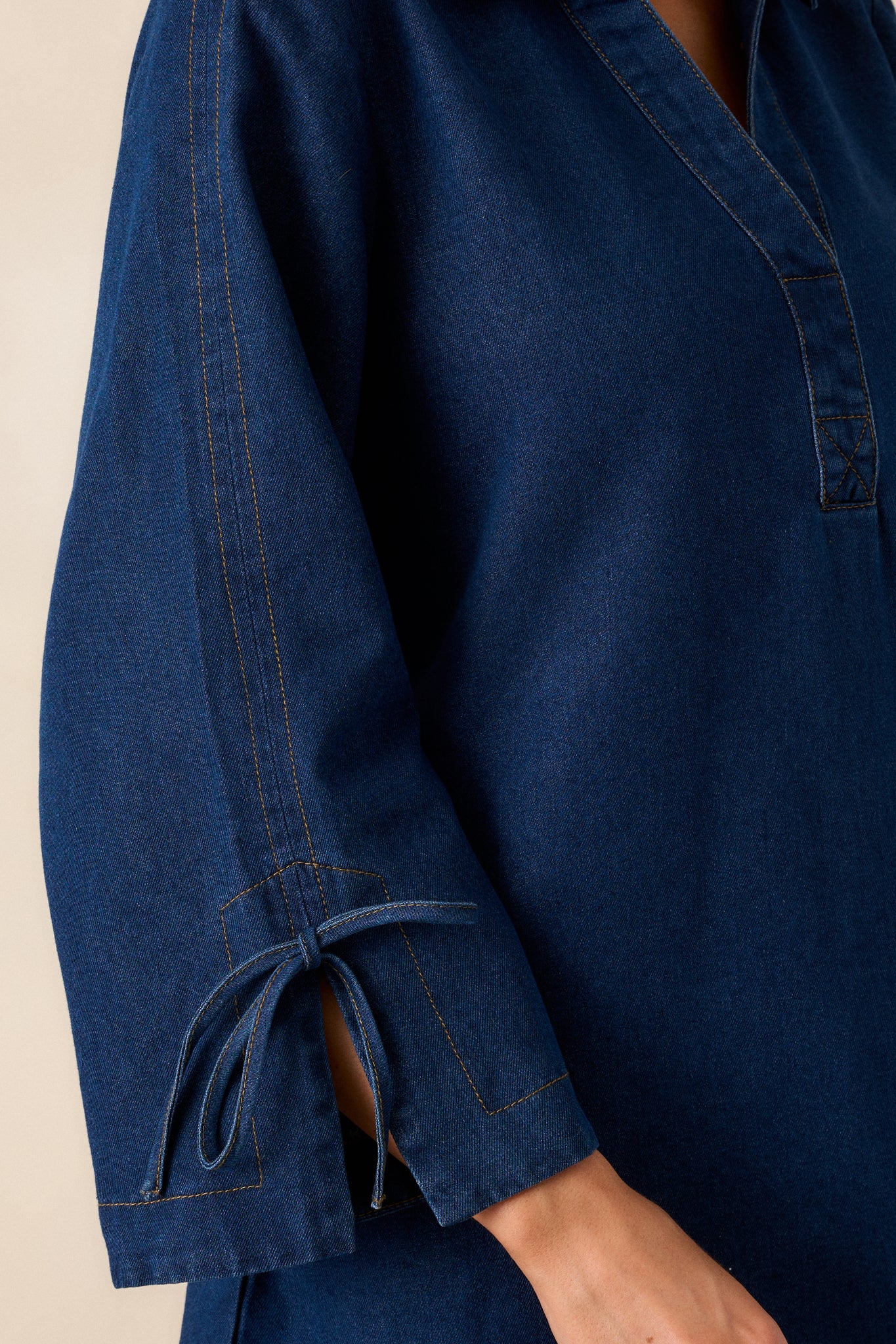 A close-up of the bow tied sleeve detail, showcasing the adjustable feature and the texture of the dark wash denim.