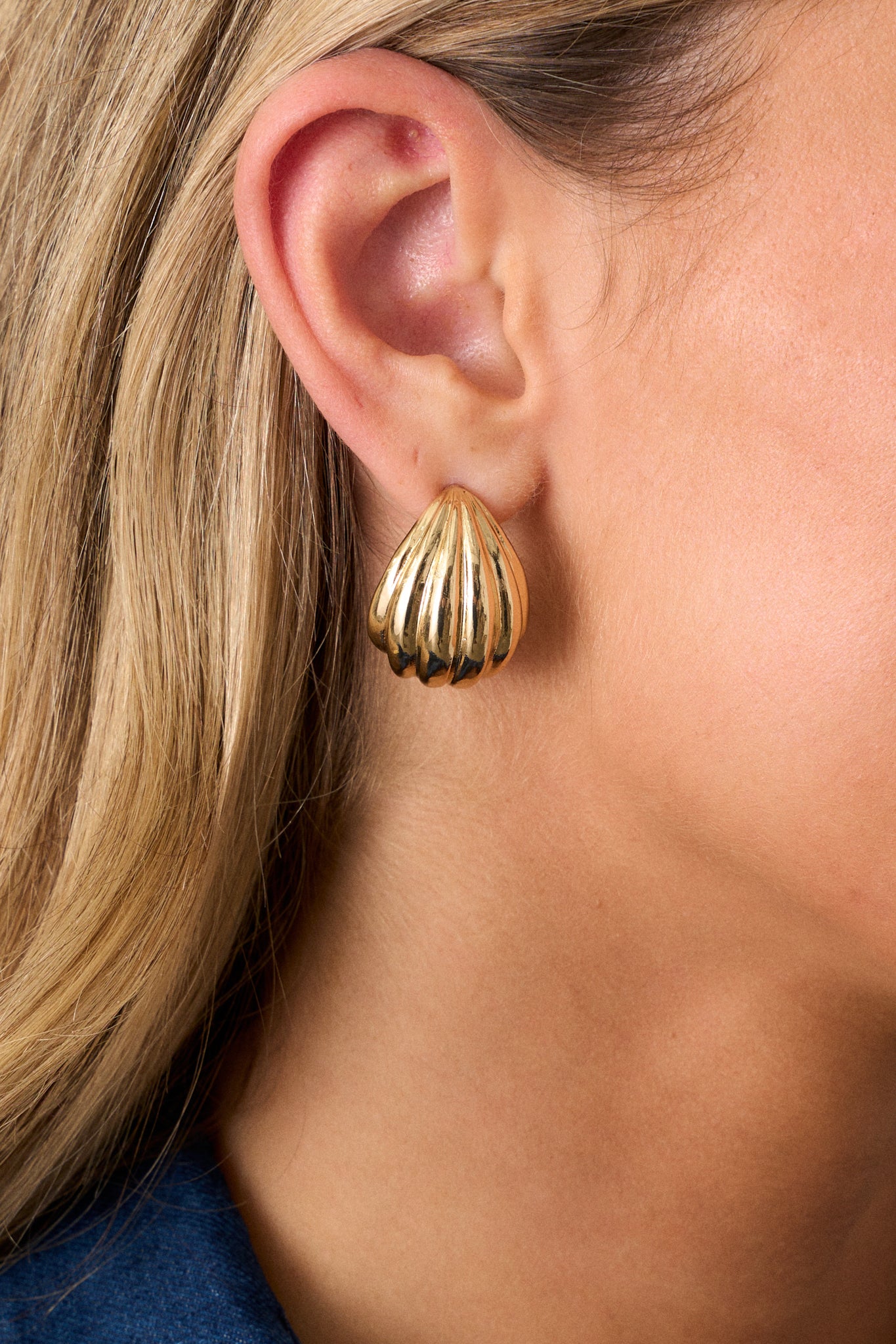 Close-up view of these earrings featuring gold hardware, a textured tear shaped stud, with secure post backings.