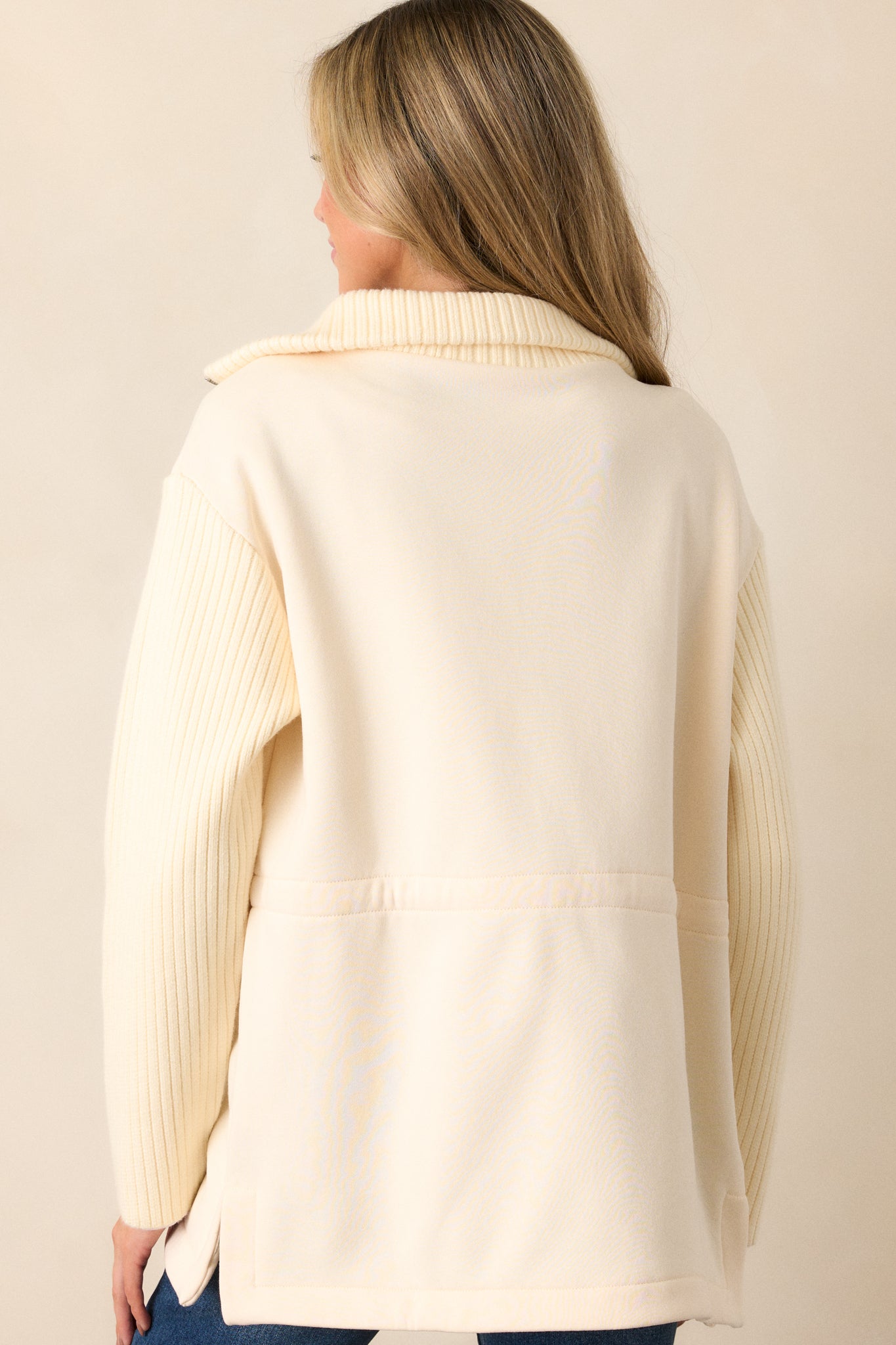 A back view of the ecru jacket, featuring the long knit sleeves and the cinched waistband, showcasing the interplay of contrasting materials.