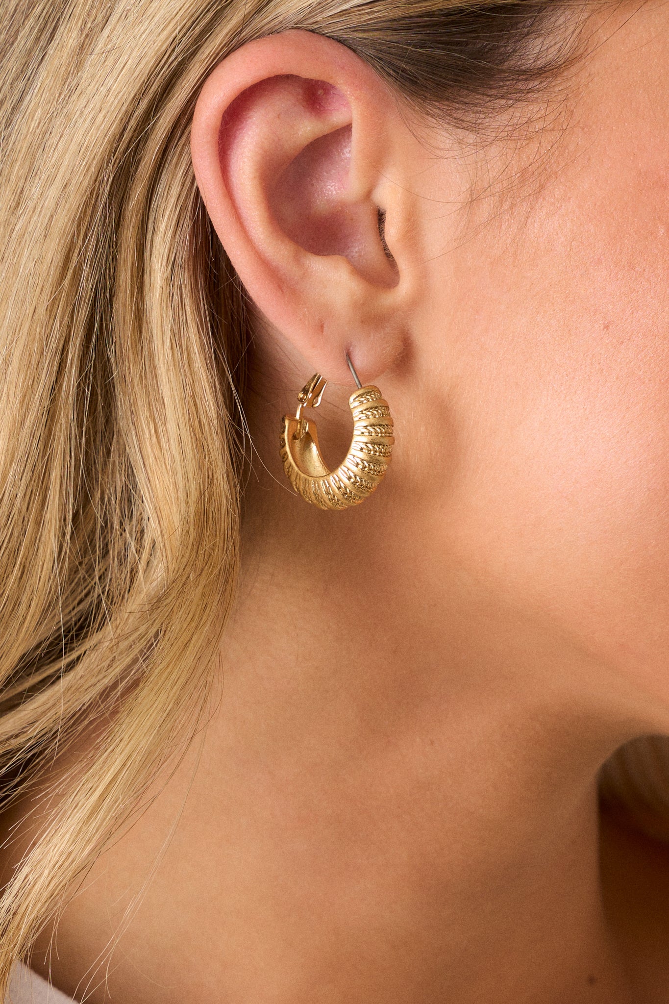 Close up view of these gold hoops that feature gold hardware, a textured ribbed design, and hinged hoop closure.