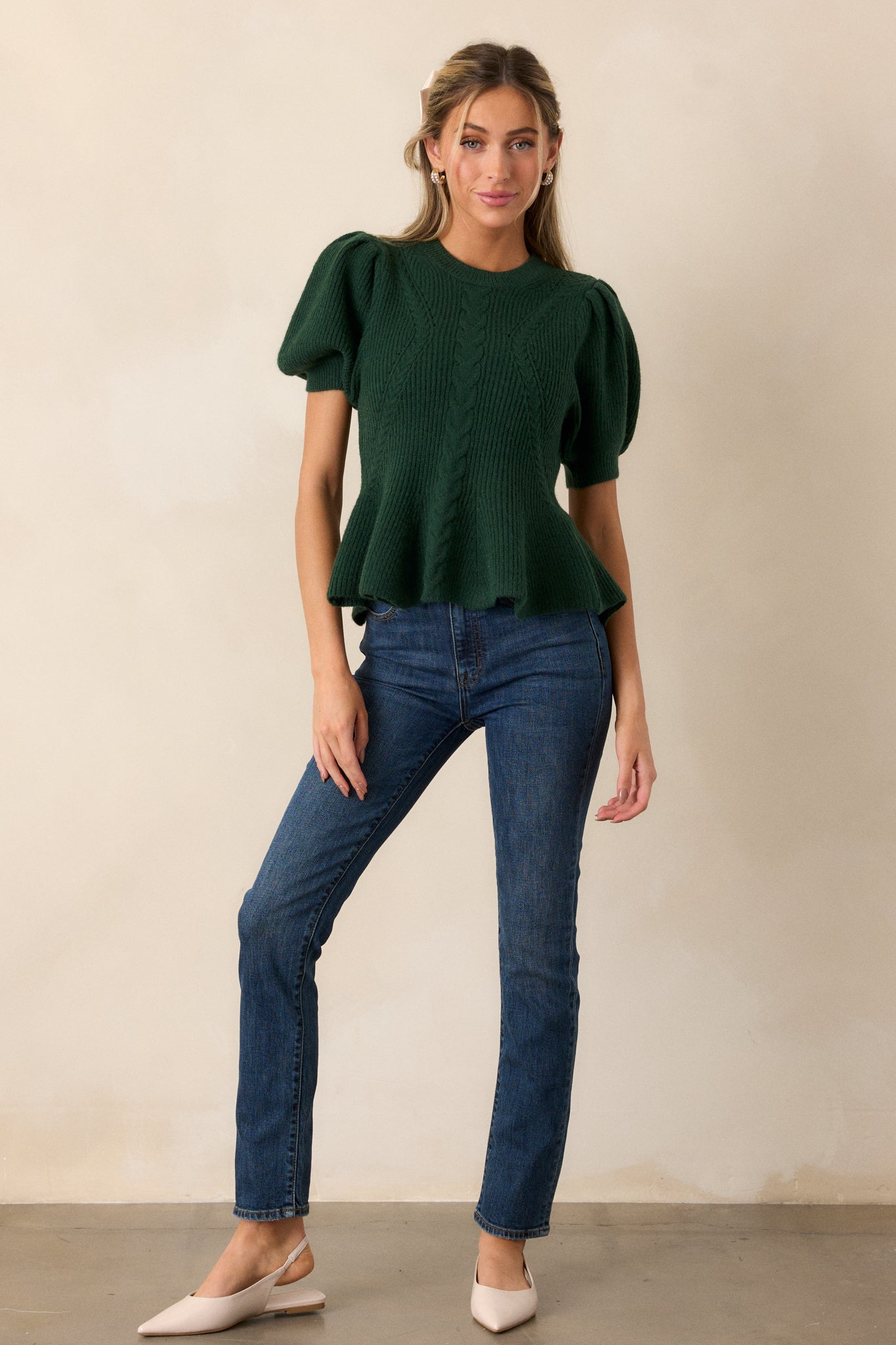 A green sweater with a rounded ribbed neckline, featuring braided knit detailing, a peplum fit, and puff sleeves with ribbed cuffs.