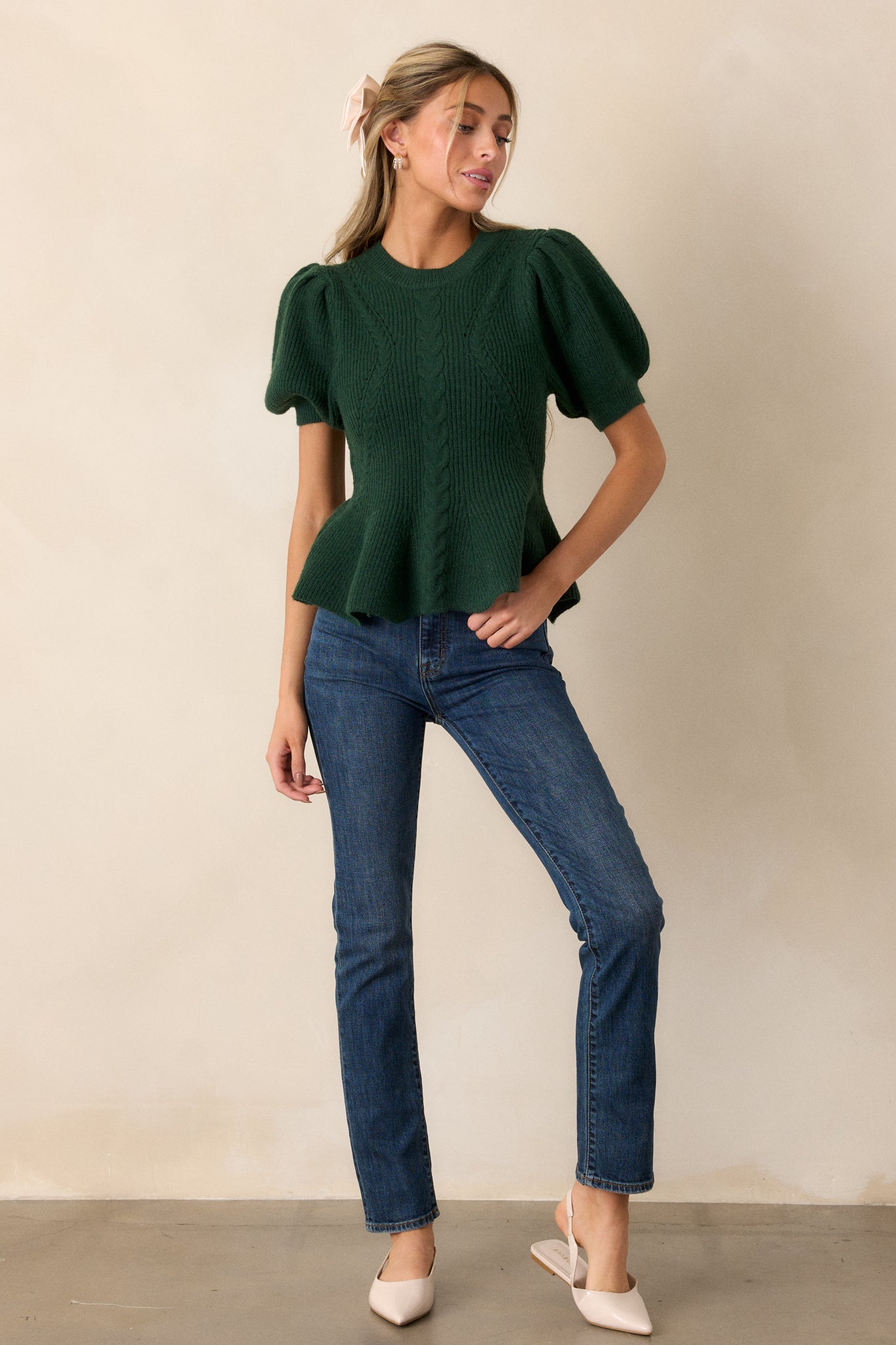 A front-facing shot of the green sweater, showcasing the rounded ribbed neckline and peplum waistline with braided knit detailing.