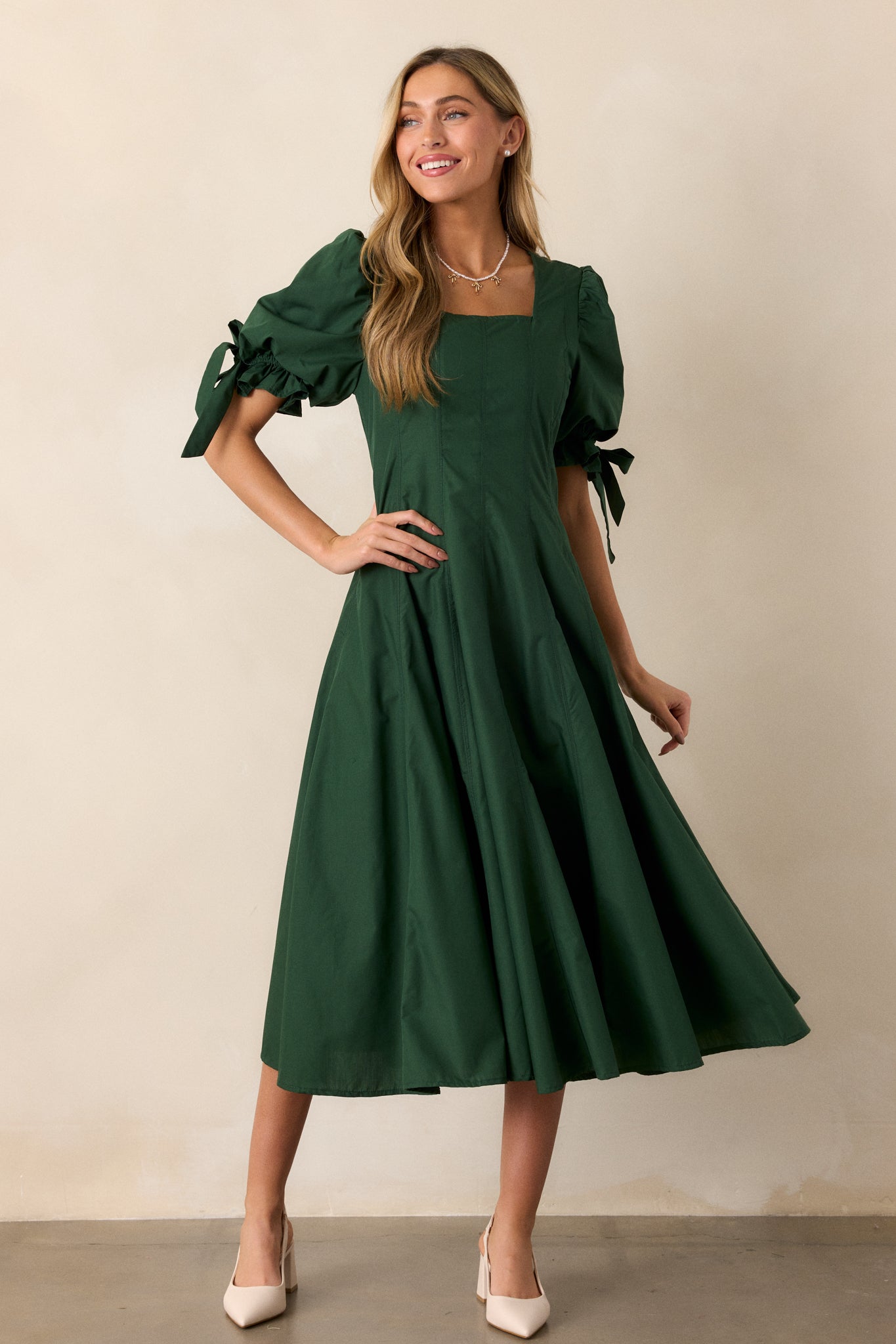 A green midi dress with a square neckline and a fit-and-flare silhouette, featuring short puff sleeves with bow accents and smocked details.