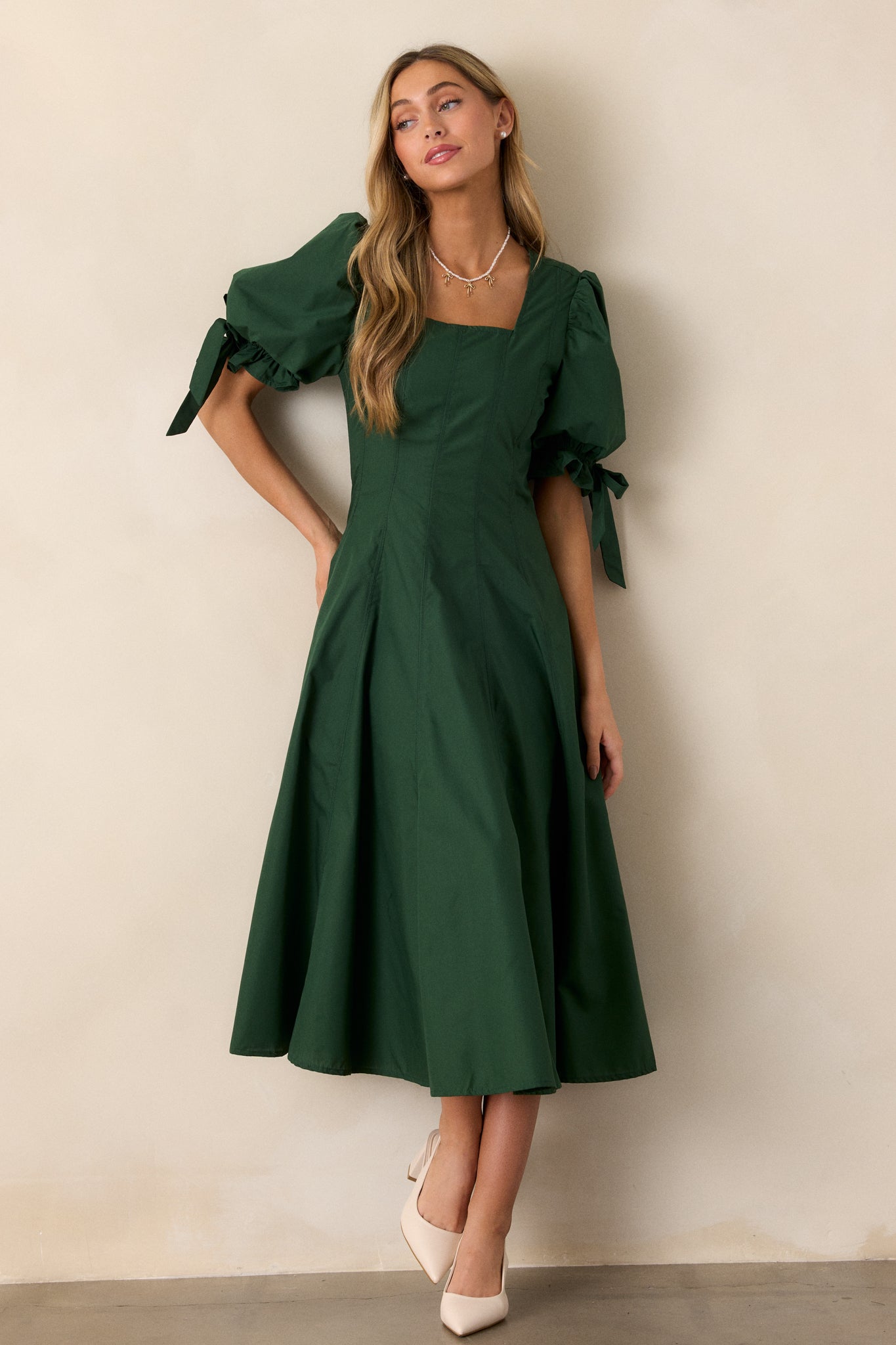 A full-body shot of the green dress, emphasizing the fit-and-flare structure, square neckline, and bow accents on the short puff sleeves.