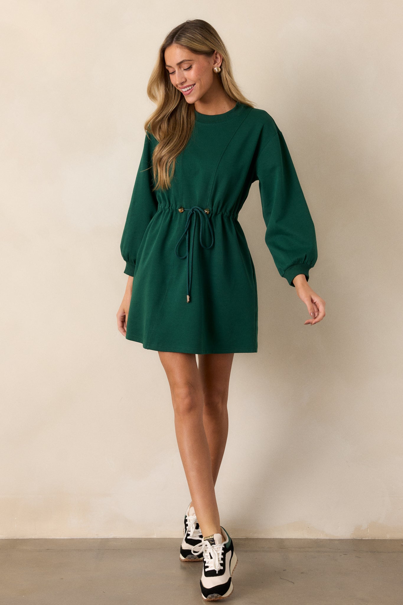 A front-facing view of the green dress, highlighting the gold heart string embellishments along the waist and the flow of the long sleeves.