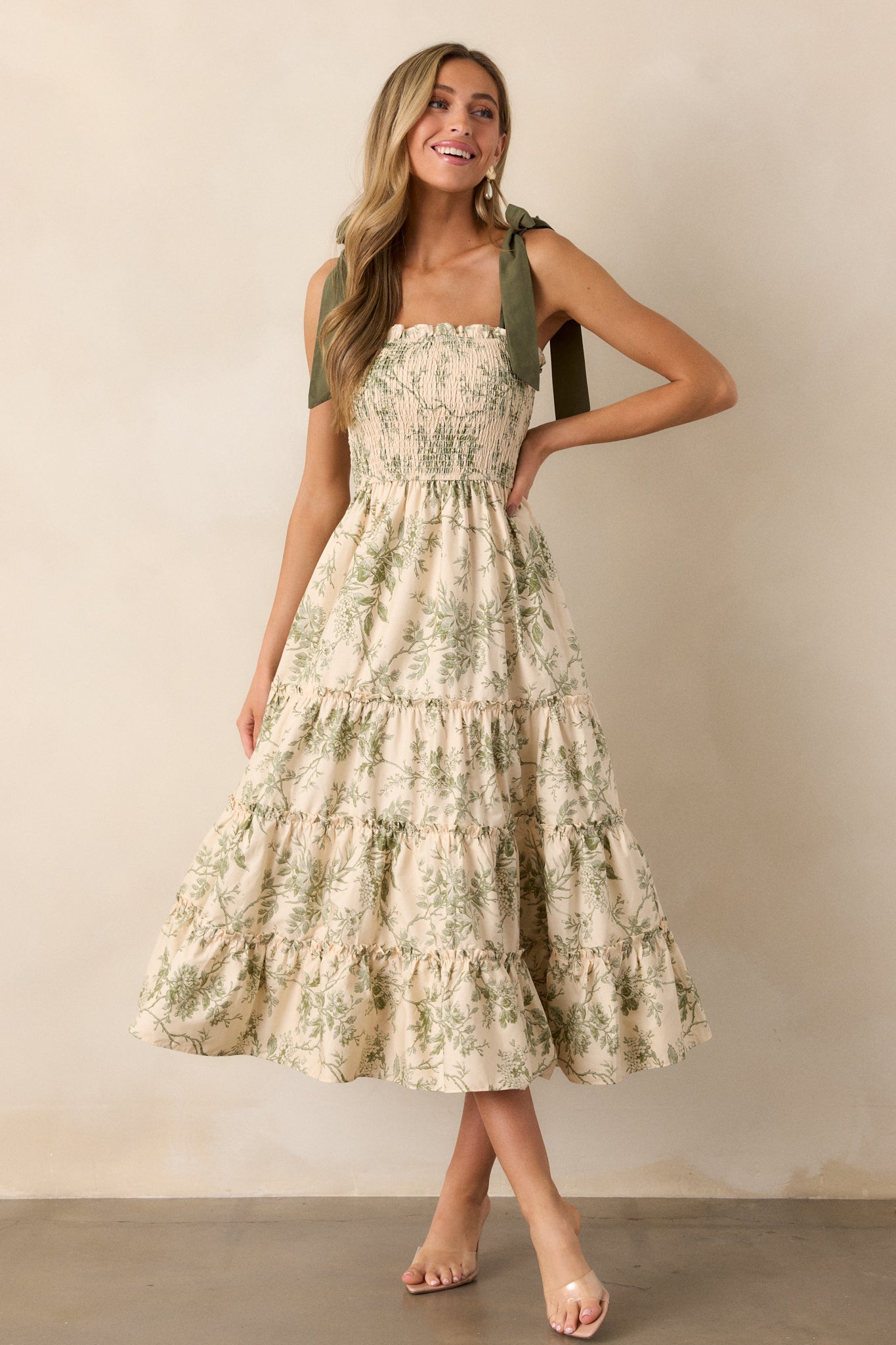 A front-facing view of the ivory dress with a green floral design, highlighting the flowy midi length and smocked top with delicate green straps.