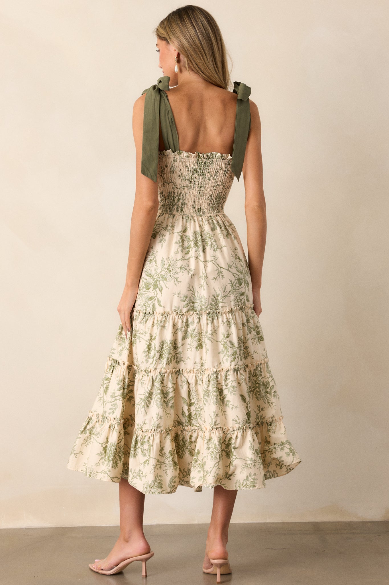 A back view of the ivory dress, showing the green floral pattern, the smocked back detail, and the green ribbon straps tied at the shoulders.