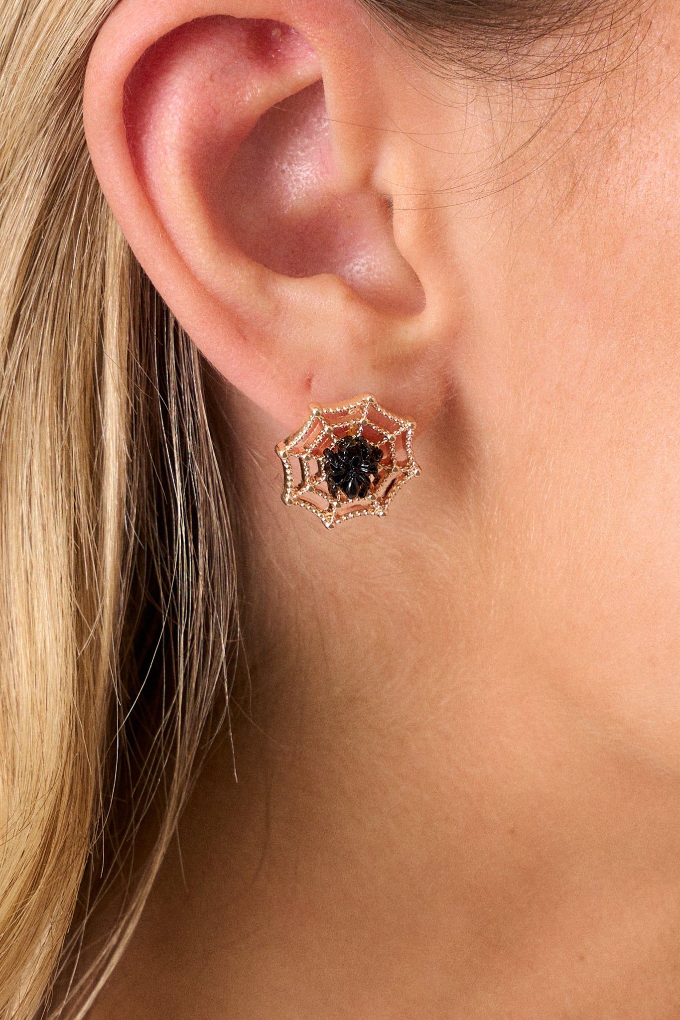 A close-up of the earrings focusing on the small black spider against the gold textured web, capturing the fine craftsmanship and the contrasting elements of the design.