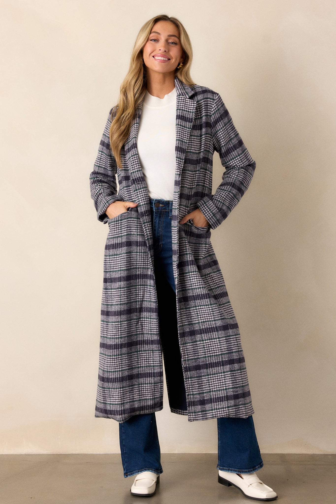 A full-body shot of the navy plaid coat, emphasizing the functional pockets, long sleeves, and button detailing on the cuffs.