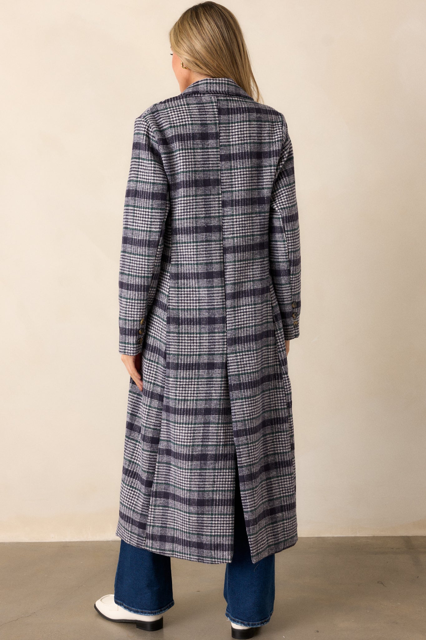 A back view of the navy plaid coat, showing the long sleeves, midi length, and the plaid design across the back.