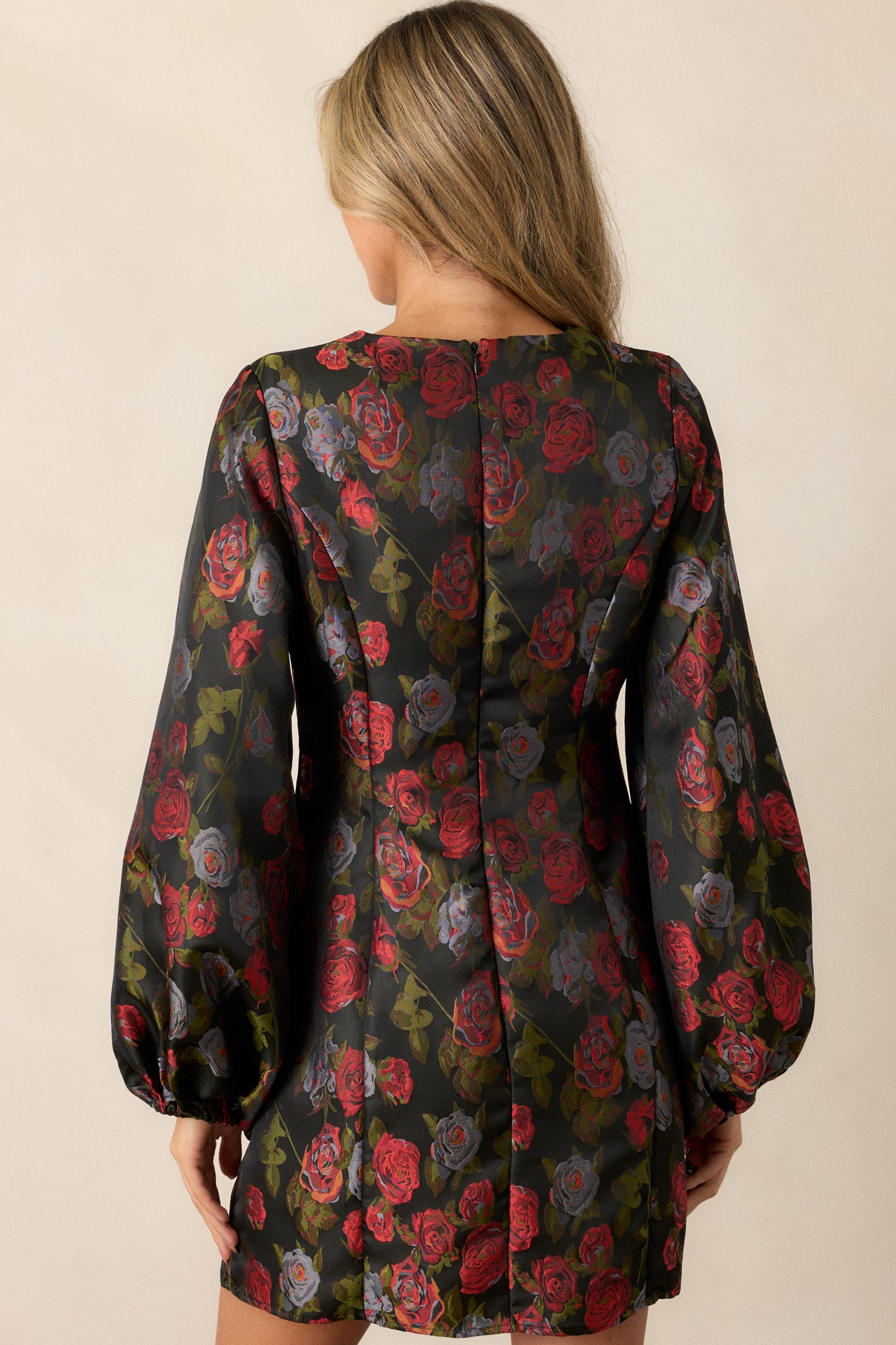 The back of the black floral dress featuring a high neckline, long puff sleeves, and a hidden zipper that maintains a smooth appearance.