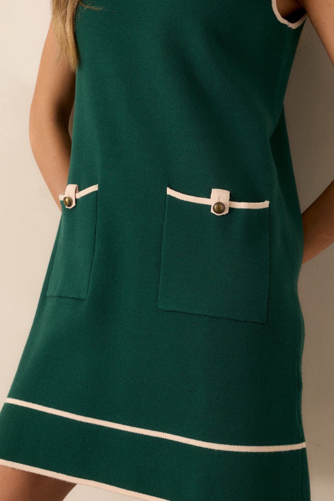 Close-up of the green dress focusing on the ribbed high neckline, gold accent buttons on the functional hip pockets, and the beige trim detailing.