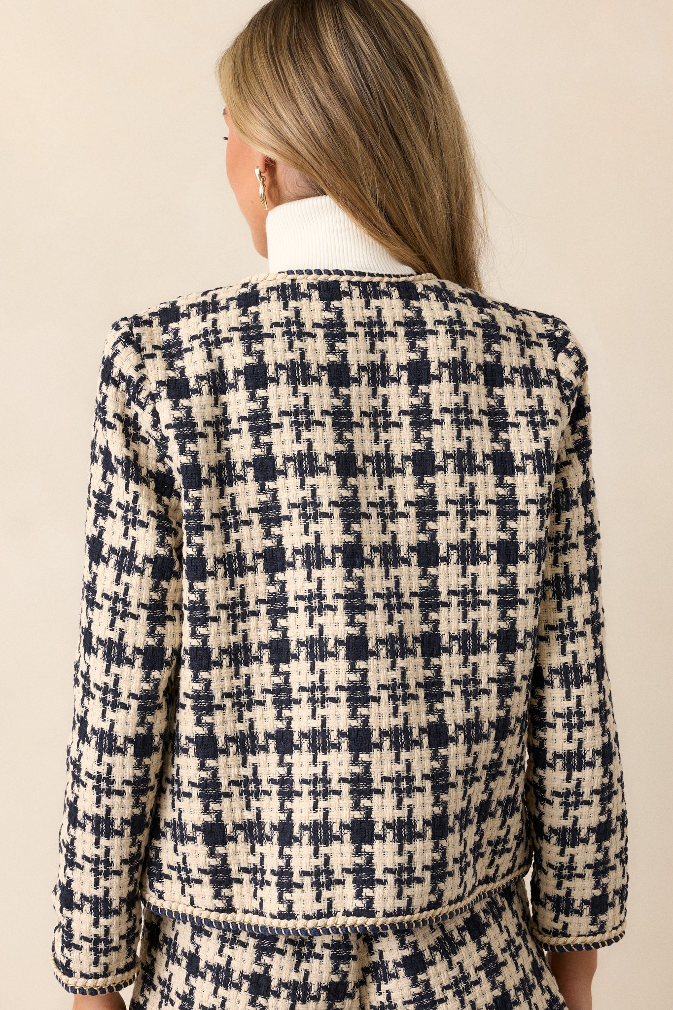 A back view of the navy tweed jacket, showing the boxy fit and the continuation of the houndstooth pattern and gold rope twist trim around the edges.