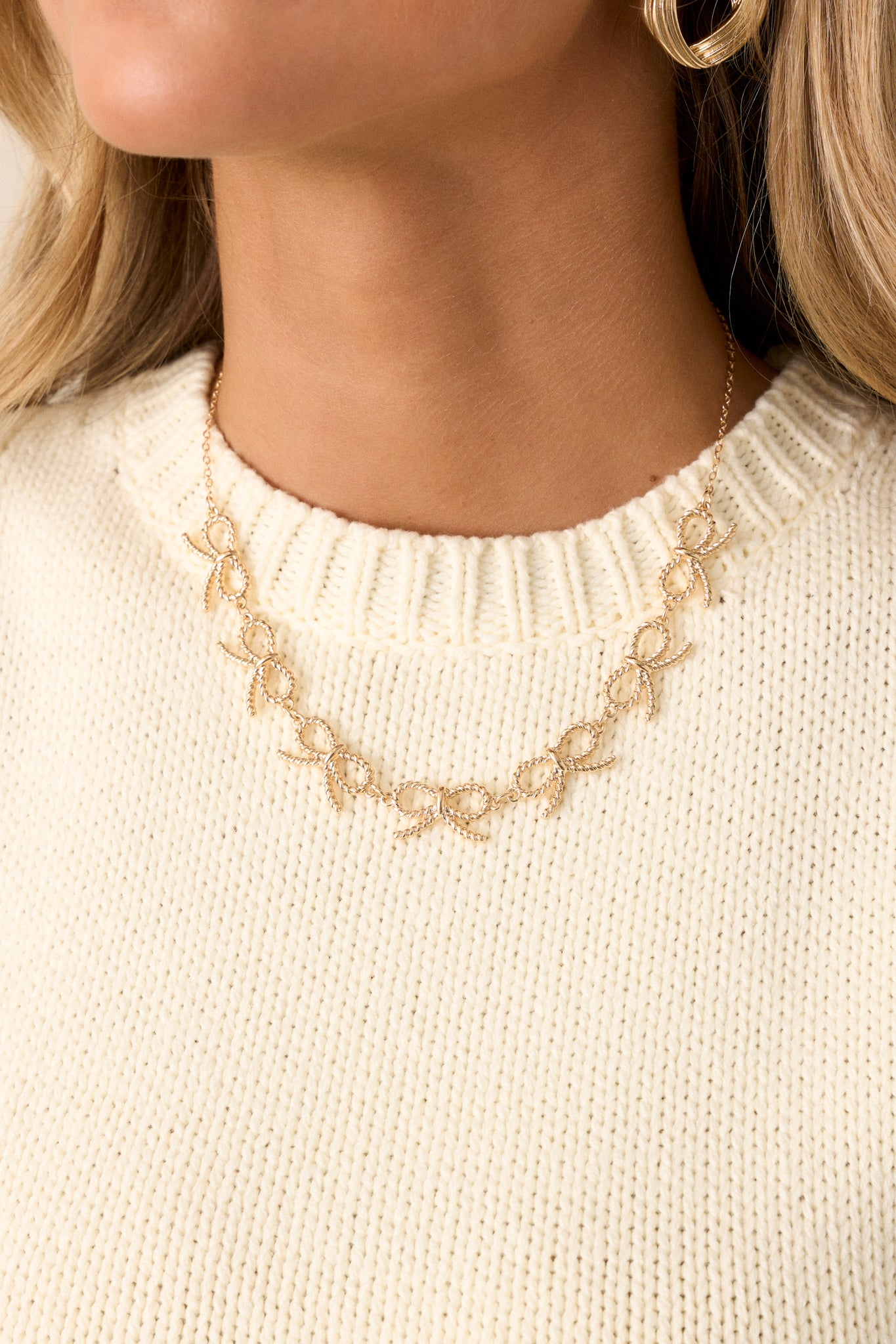 A cropped view of the gold necklace showcasing the thin gold chain and the arrangement of seven gold rope-textured bows that adorn the necklace.