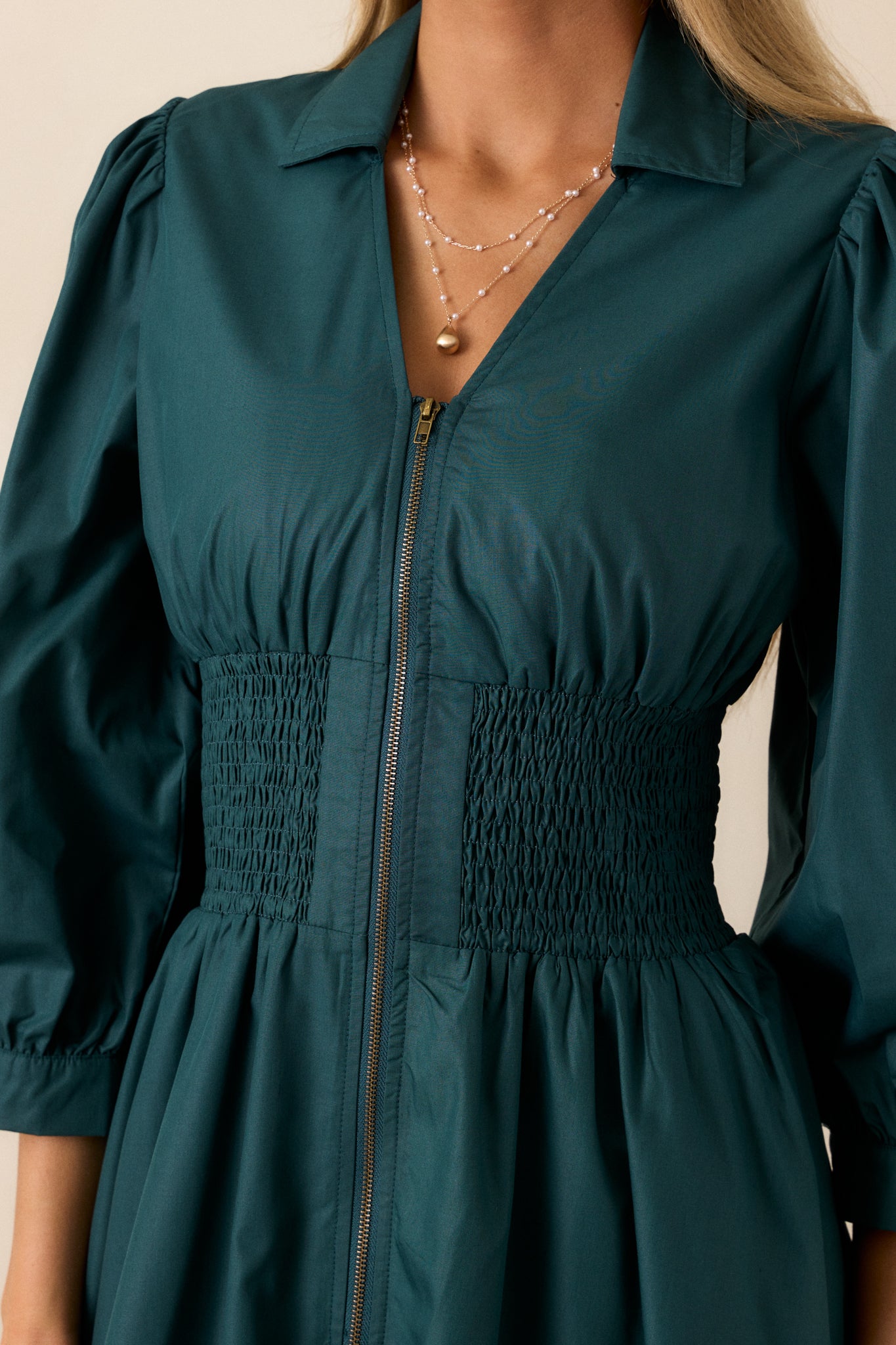 Close-up of the front zipper with brassy gold hardware, highlighting the texture of the forest green fabric and smocked waist detail.