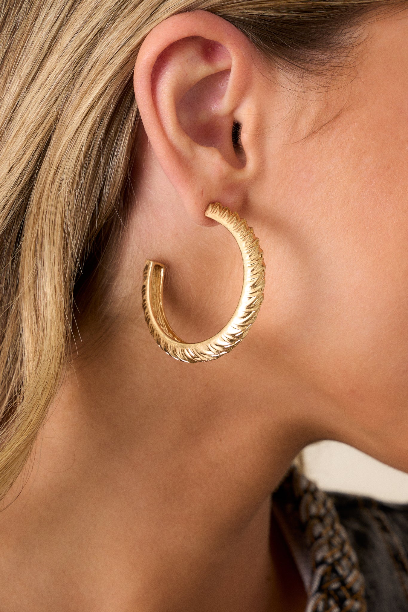 Close up view of these gold hoop earrings that feature a gold finish, a grooved textured design, and secure post backings.