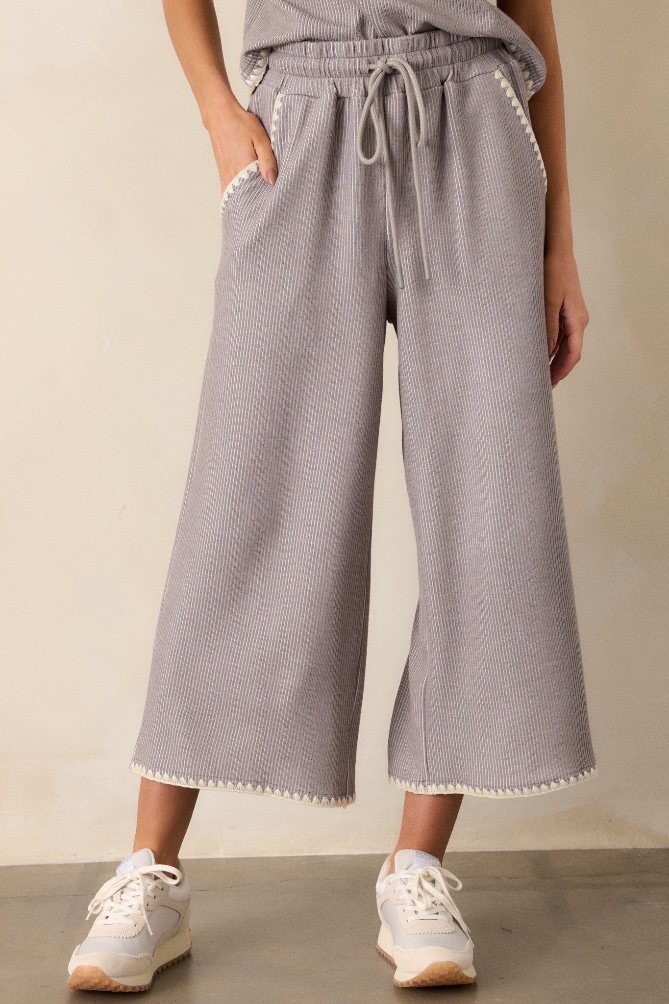 Front view of these grey pants that feature an elastic waistband, an optional waist drawstring, an ivory ruffle trim, functional hip pockets, a soft stitched material and a wide leg