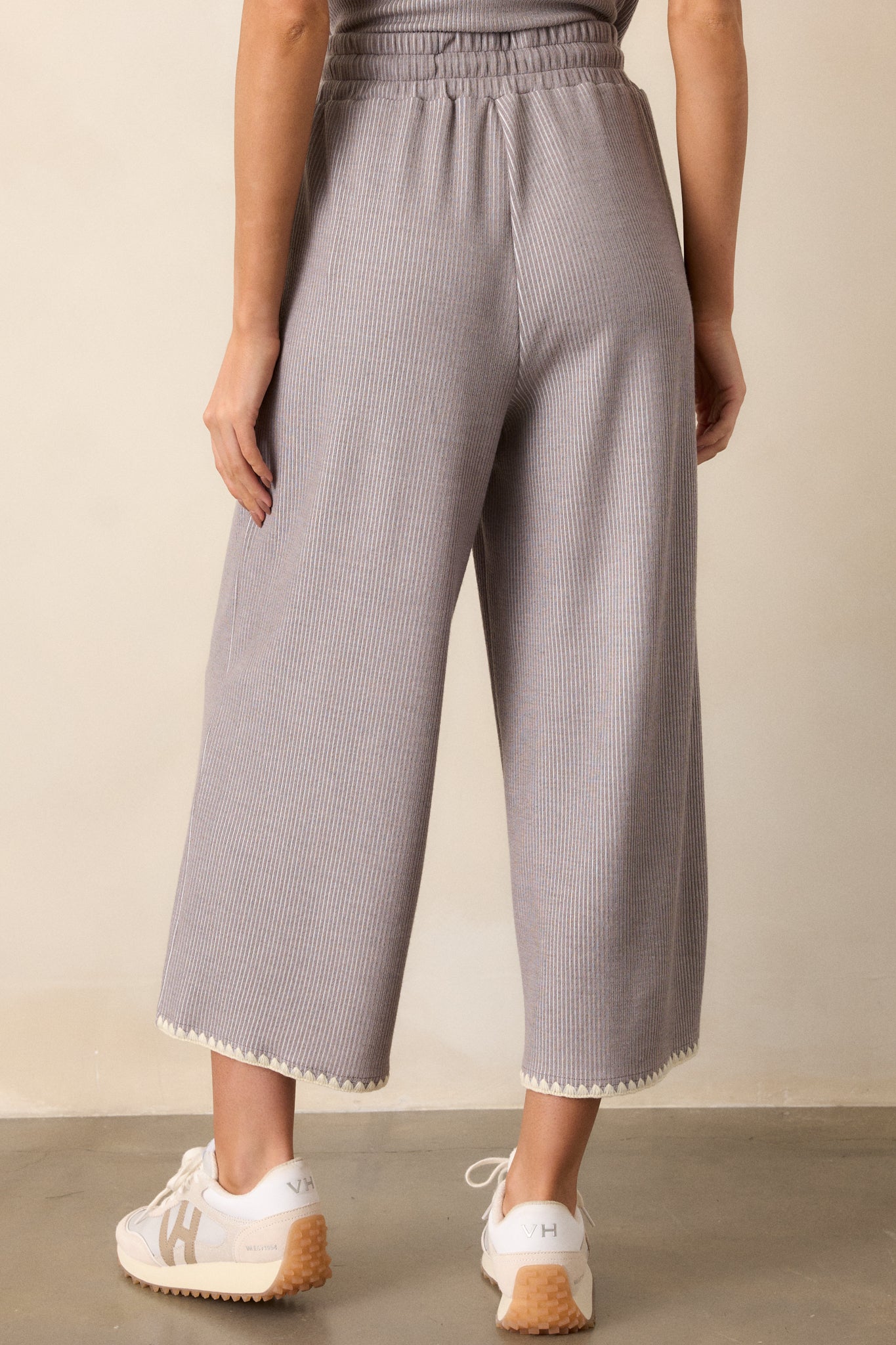 Back of these grey pants that feature an elastic waistband, an optional waist drawstring, an ivory ruffle trim, functional hip pockets, a soft stitched material and a wide leg