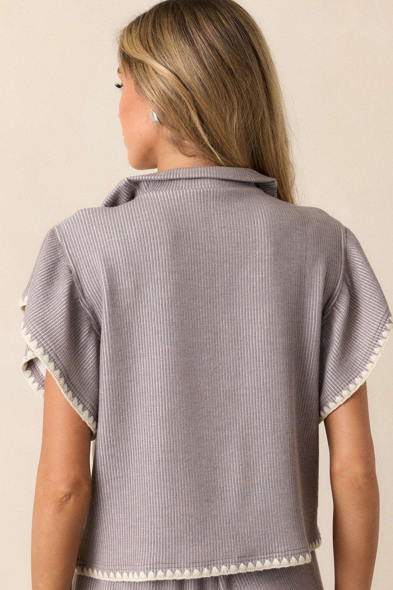 Back view of this grey sweater that features a collared quarter zip neckline, a relaxed fit, a soft knit material, flutter sleeves, and ivory blanket stitch detailing.