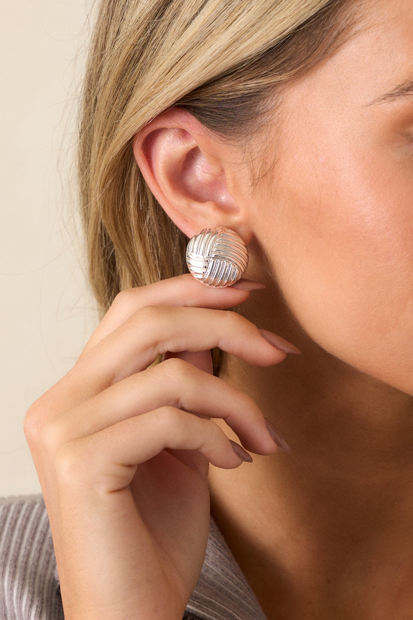 A cropped view of the earrings showcasing the circular shape and quilted wave-like pattern of the silver hardware, emphasizing their elegant design.