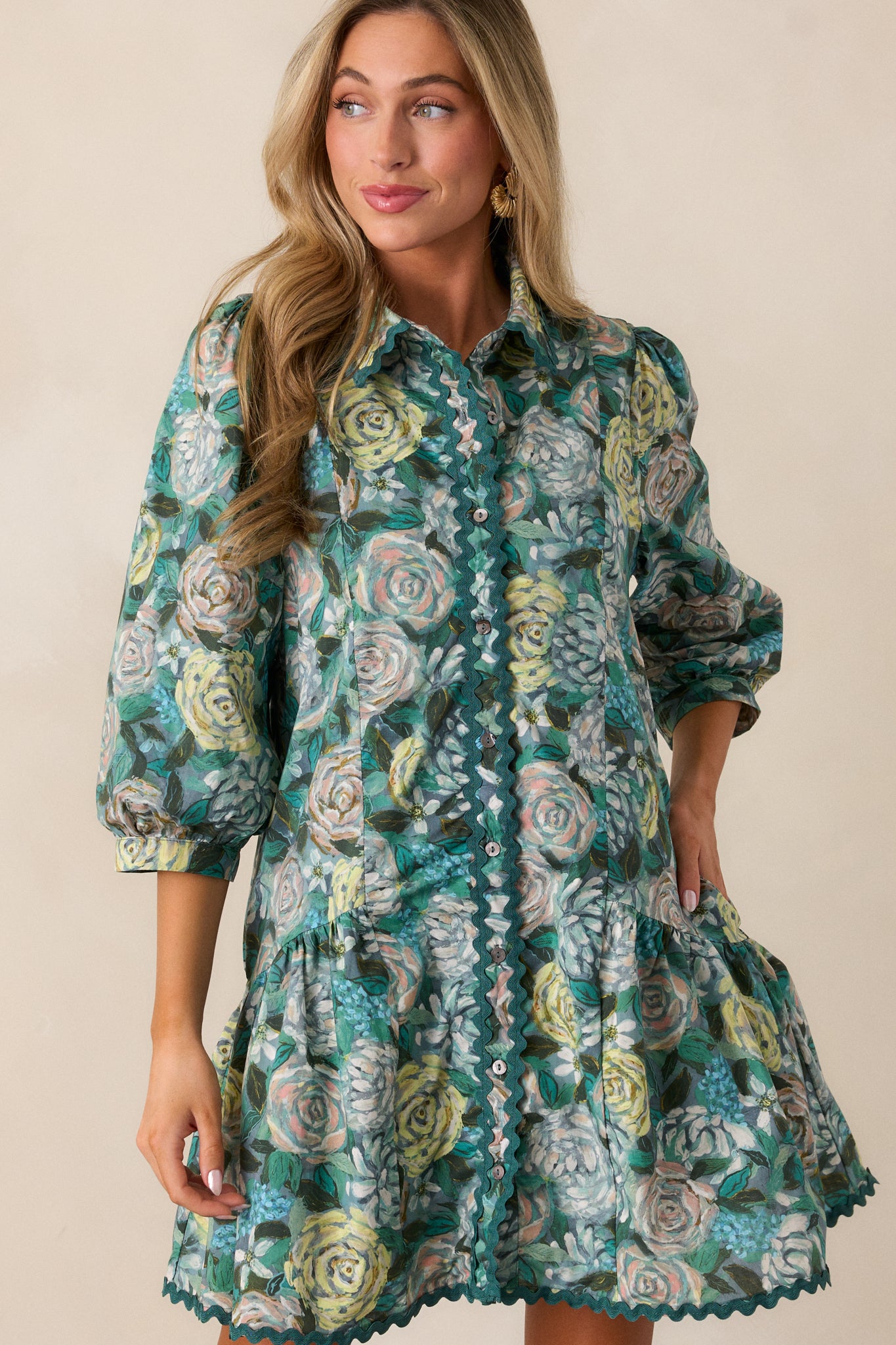 A second full-body shot highlighting the collared neckline with green ricrac lining, button front, and the dress’s overall shape. The floral pattern and tiered bottom are visible, along with the 3/4 sleeves.