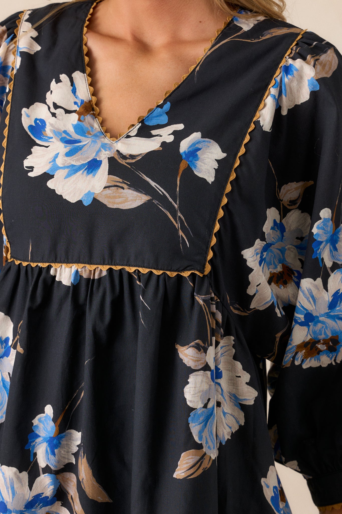 Close-up of the tan stitching on the black dress, emphasizing the intricate stitchwork against the floral pattern.