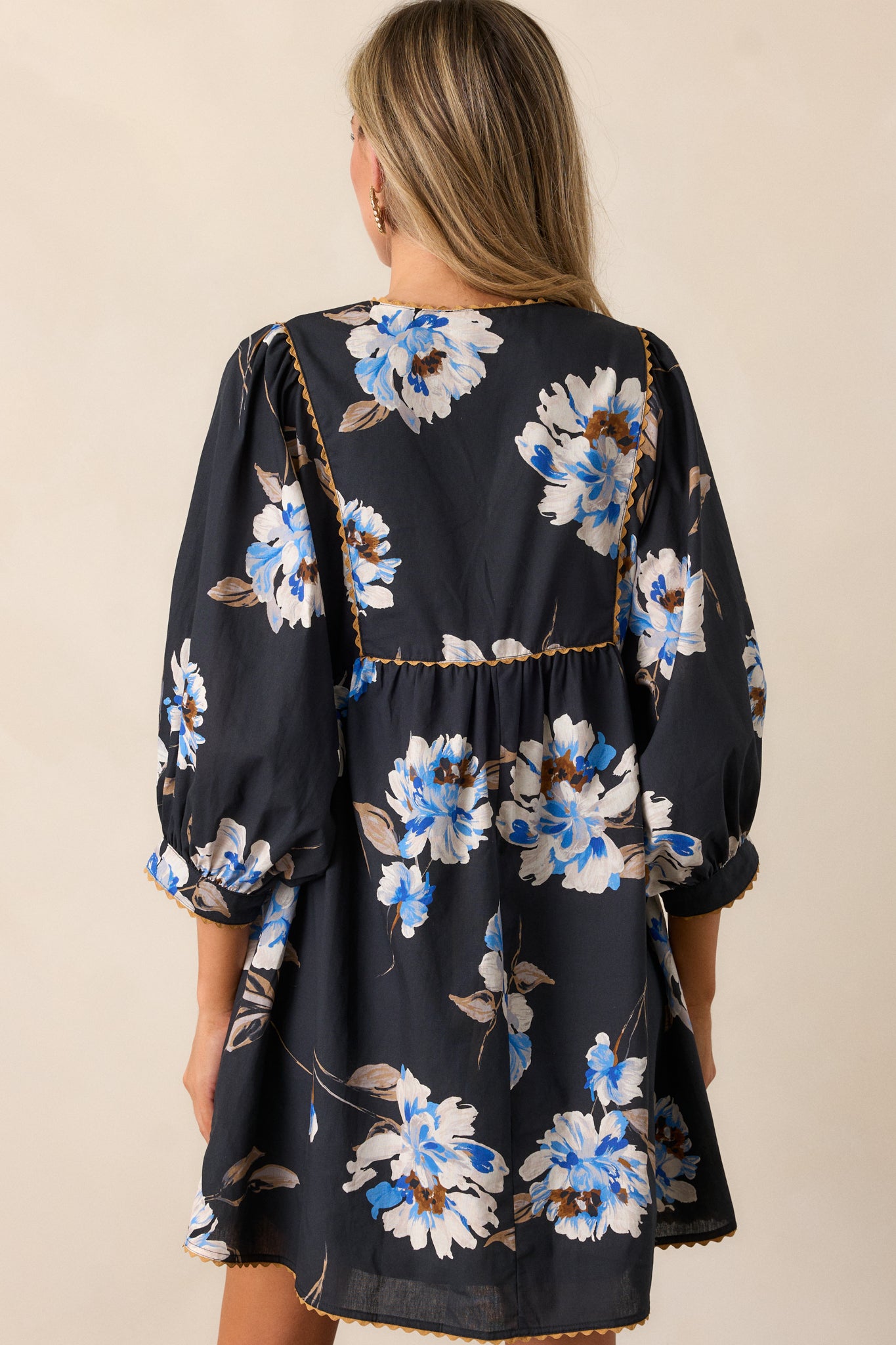 Back view of the black mini dress, showing the blue and white floral design across the fabric and tan stitching detail on the 3/4 sleeves.