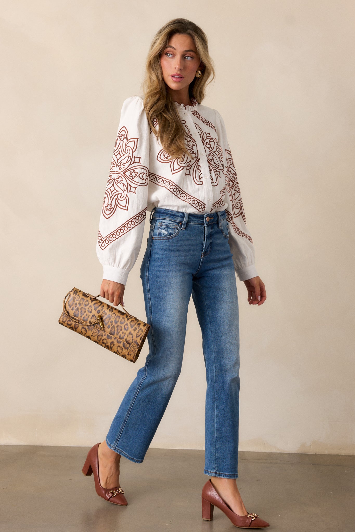 Ivory blouse featuring a high ruffled neckline and long sleeves, highlighting the relaxed fit with camel stitching along the button front.