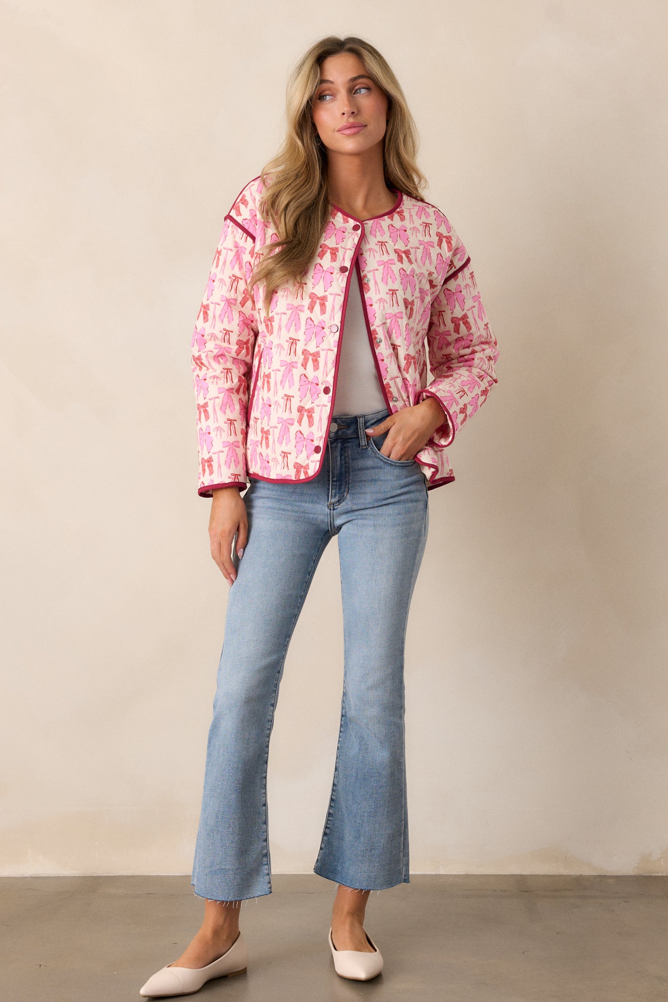 Front view of the pink blue jacket, showcasing the snap button front, round neckline, and multicolor bow print across the quilted fabric.