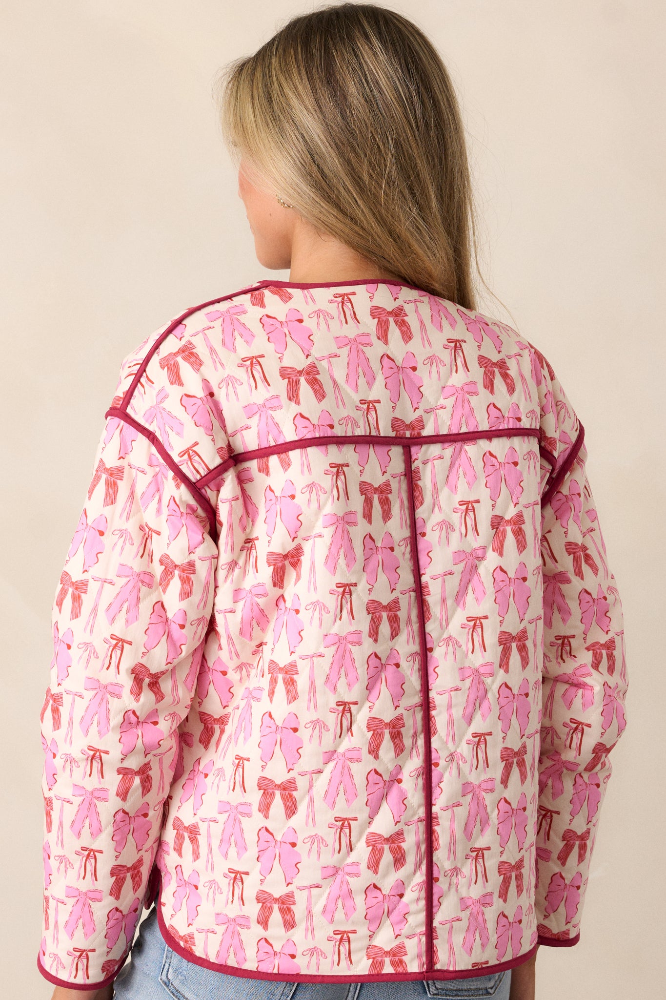 Back view of the jacket, displaying the all-over bow print, quilted design, and the blue trim along the back hemline and cuffs.