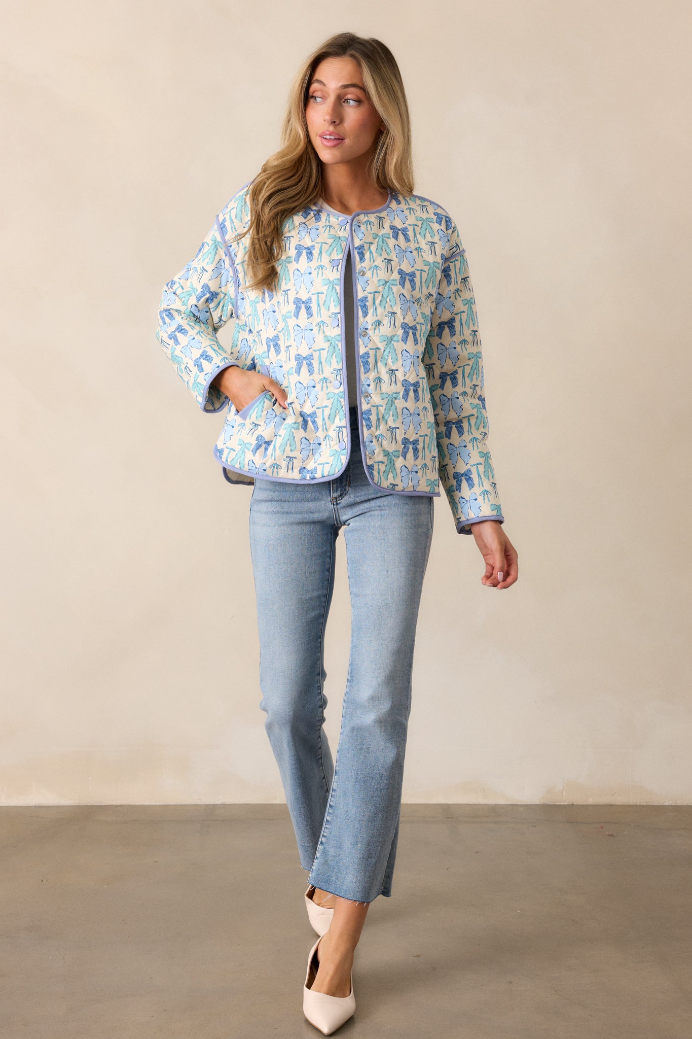 Front view of the sky blue jacket, displaying the functional snap button front, round neckline, and multicolor bow print across the quilted material.