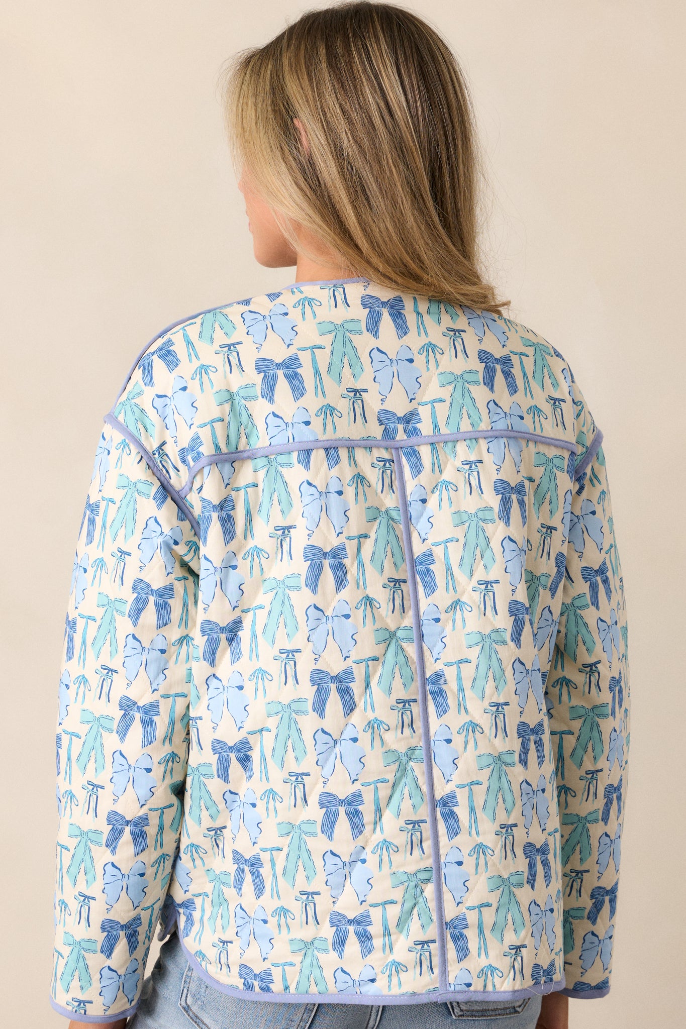 Back view of the jacket, displaying the consistent bow print, quilting, and the blue trim along the hem and cuffs.