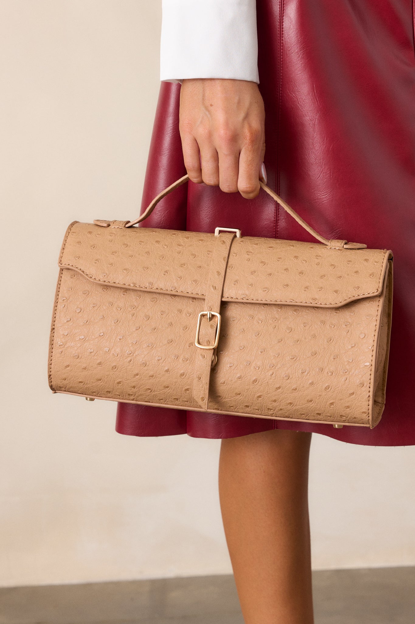 A front view of the camel handbag, highlighting the ostrich print texture, small matching handle, and gold hardware with the optional shoulder strap attached.