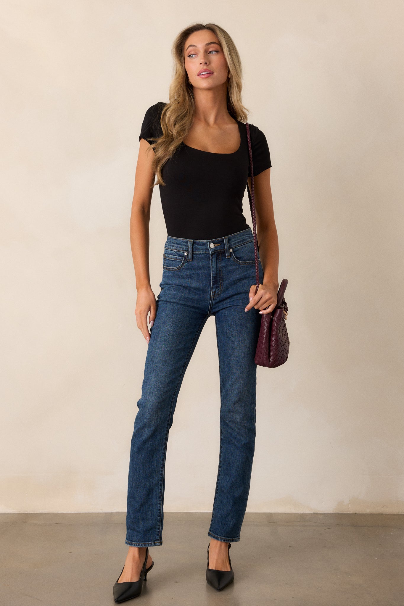 Full length view of a model wearing the black bodysuit, featuring a scoop neckline, short sleeves, and a fitted silhouette, with bottom snap button closures