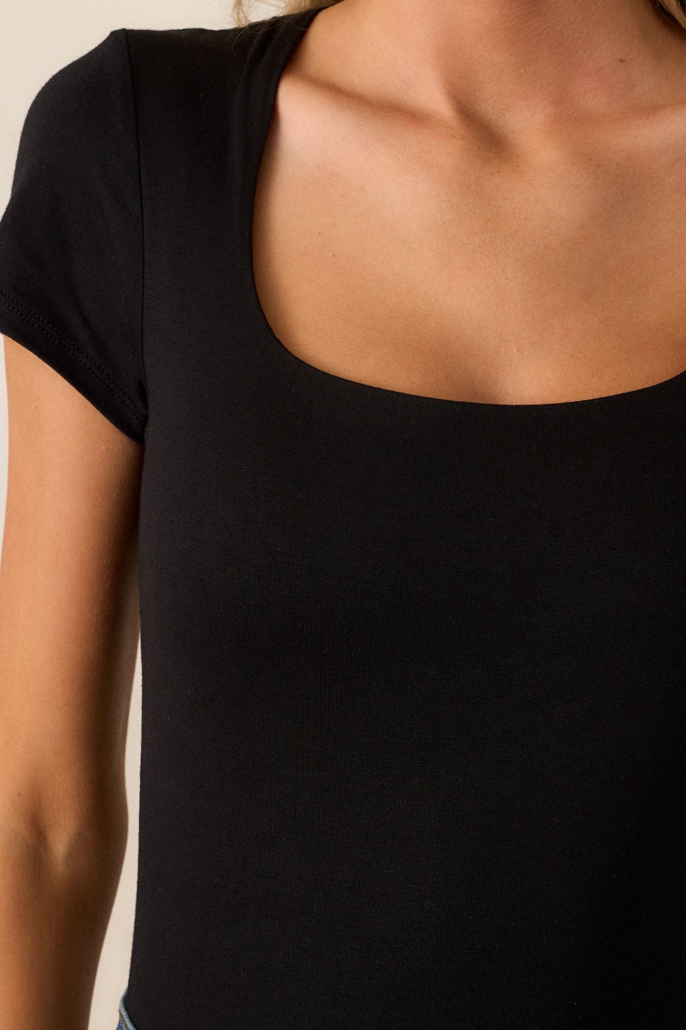 Close-up of the black bodysuit focusing on the scoop neckline, the short sleeves, and the fabric texture