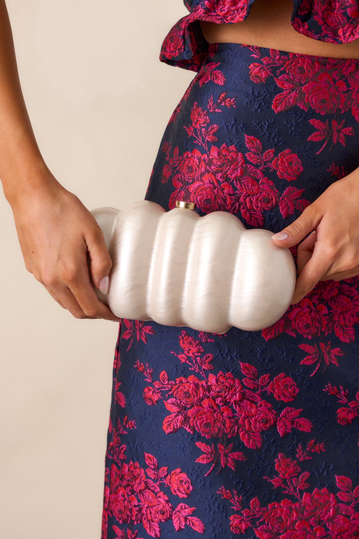 Full view of the ivory clutch with a cloud-like oval shape and an ivory pearlescent color, featuring a gold and ivory tuck lock at the top.