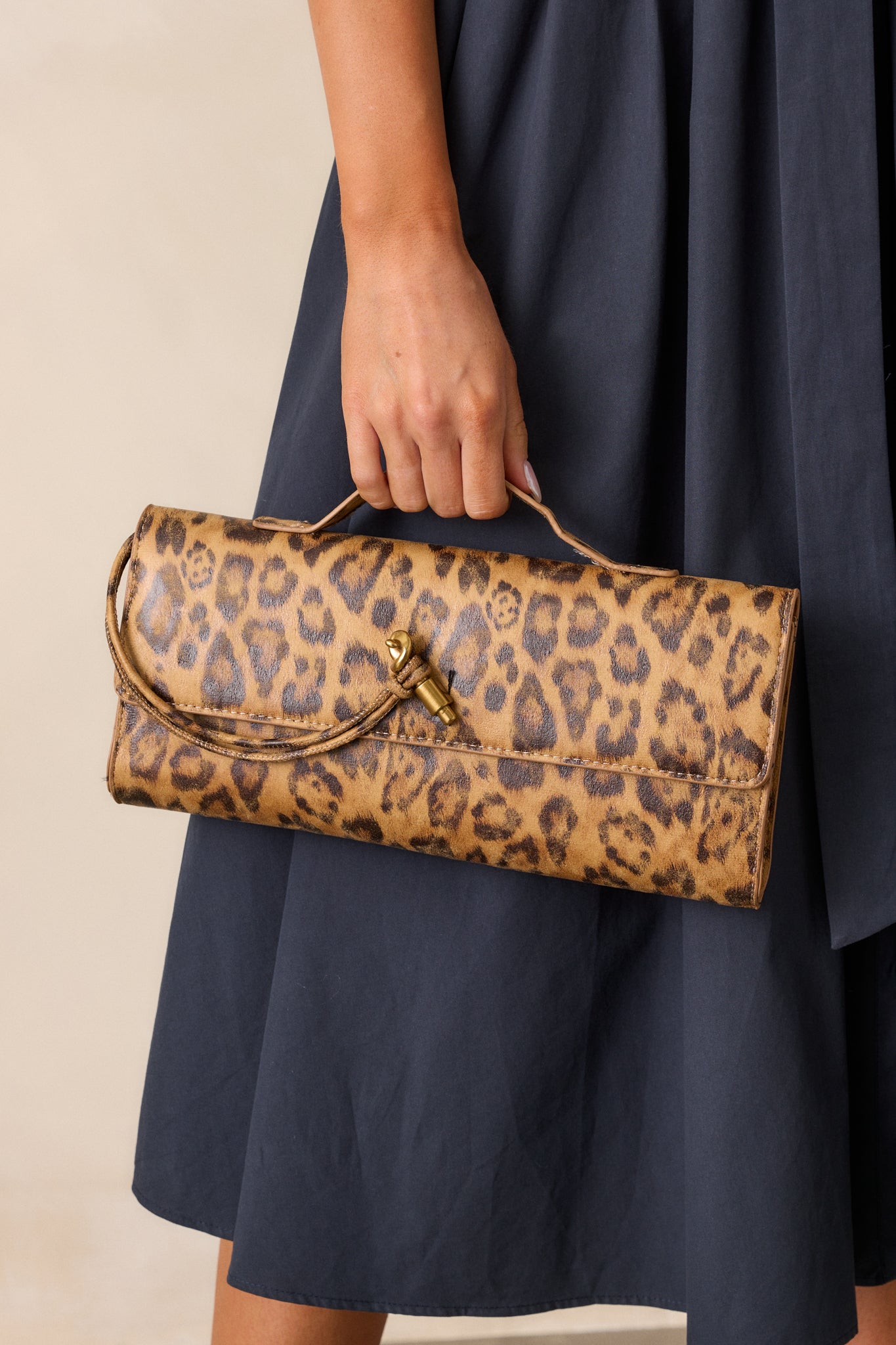 Full view of the leopard handbag, showing its rectangular shape, top handle, and gold hardware against the sleek surface.