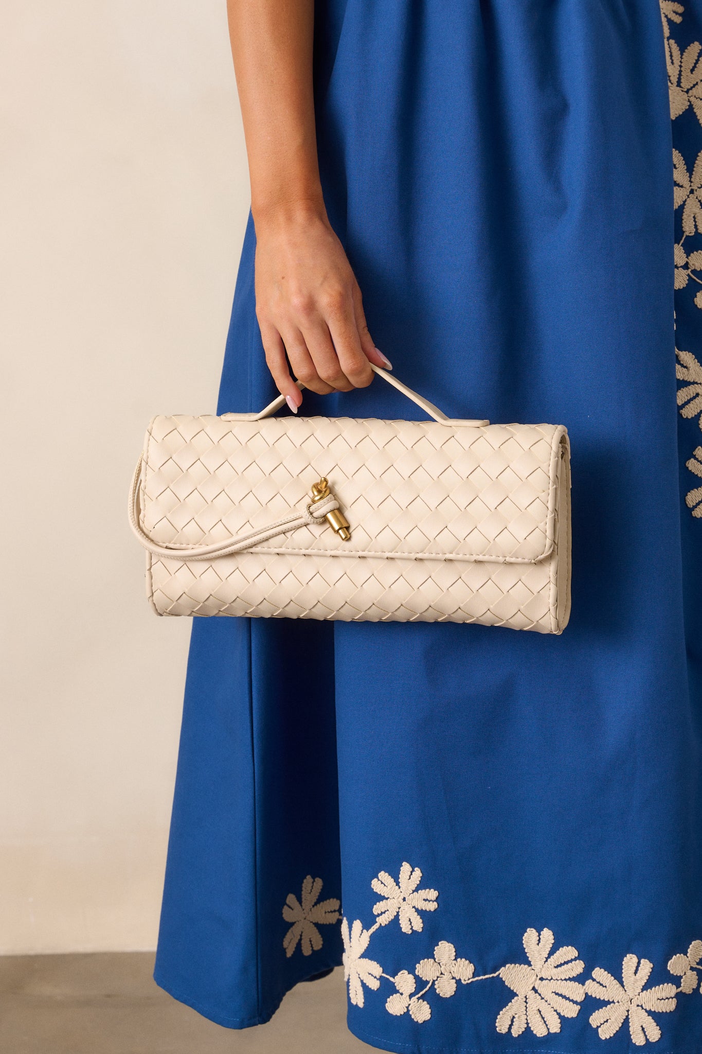 Full view of the ivory handbag, showing its rectangular shape, top handle, and gold hardware against the sleek surface.