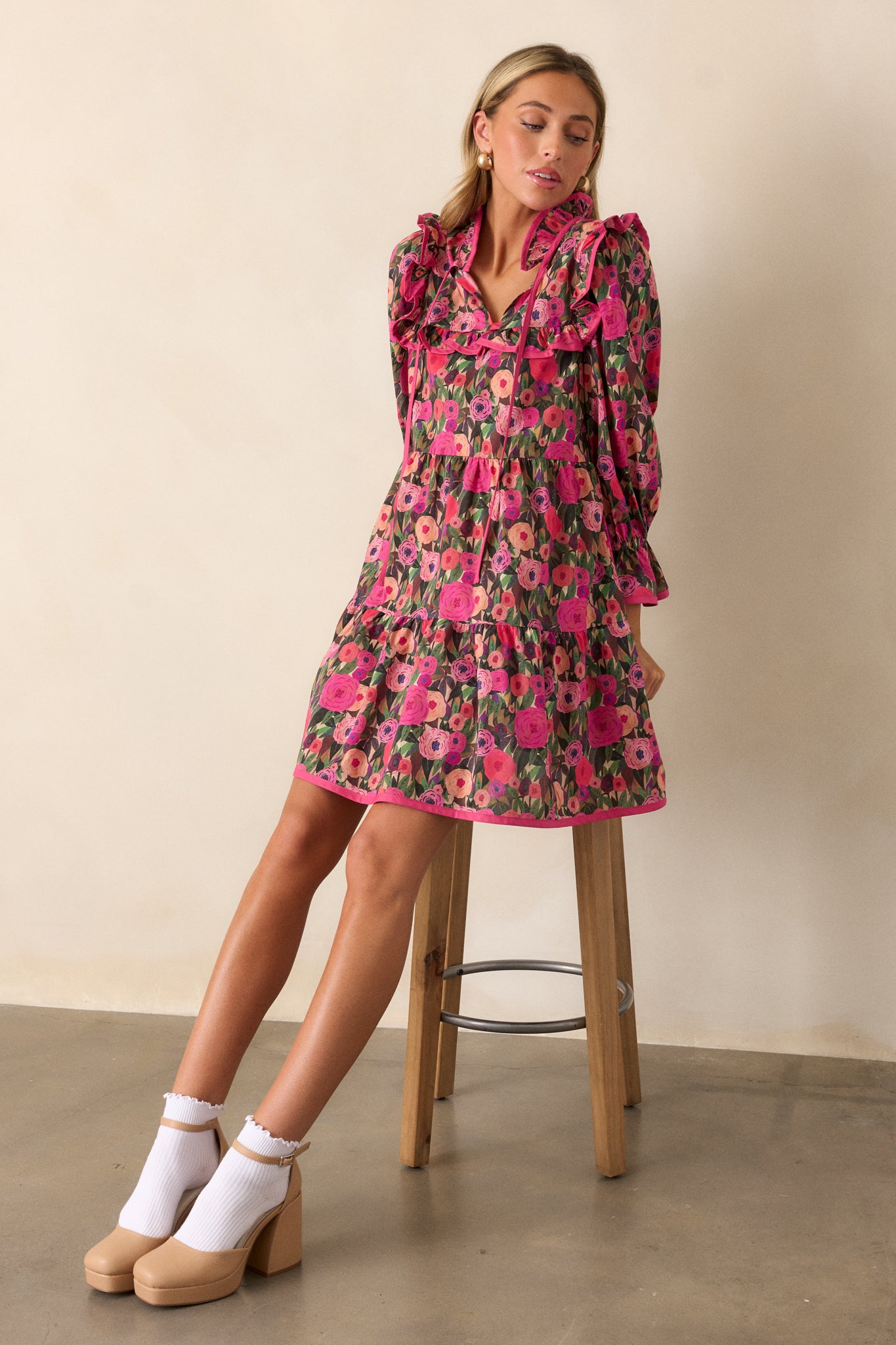 Front view of a pink floral mini dress with long sleeves, ruffled shoulder details, and pink seams.