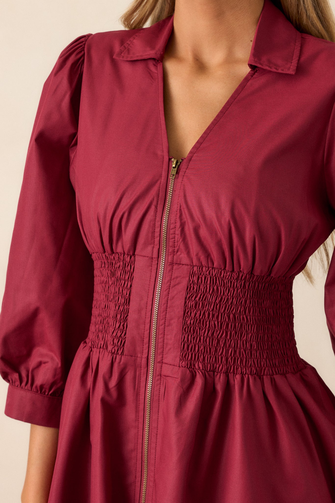 Close-up of the front zipper with brassy gold hardware, highlighting the texture of the dark sangria fabric and smocked waist detail.