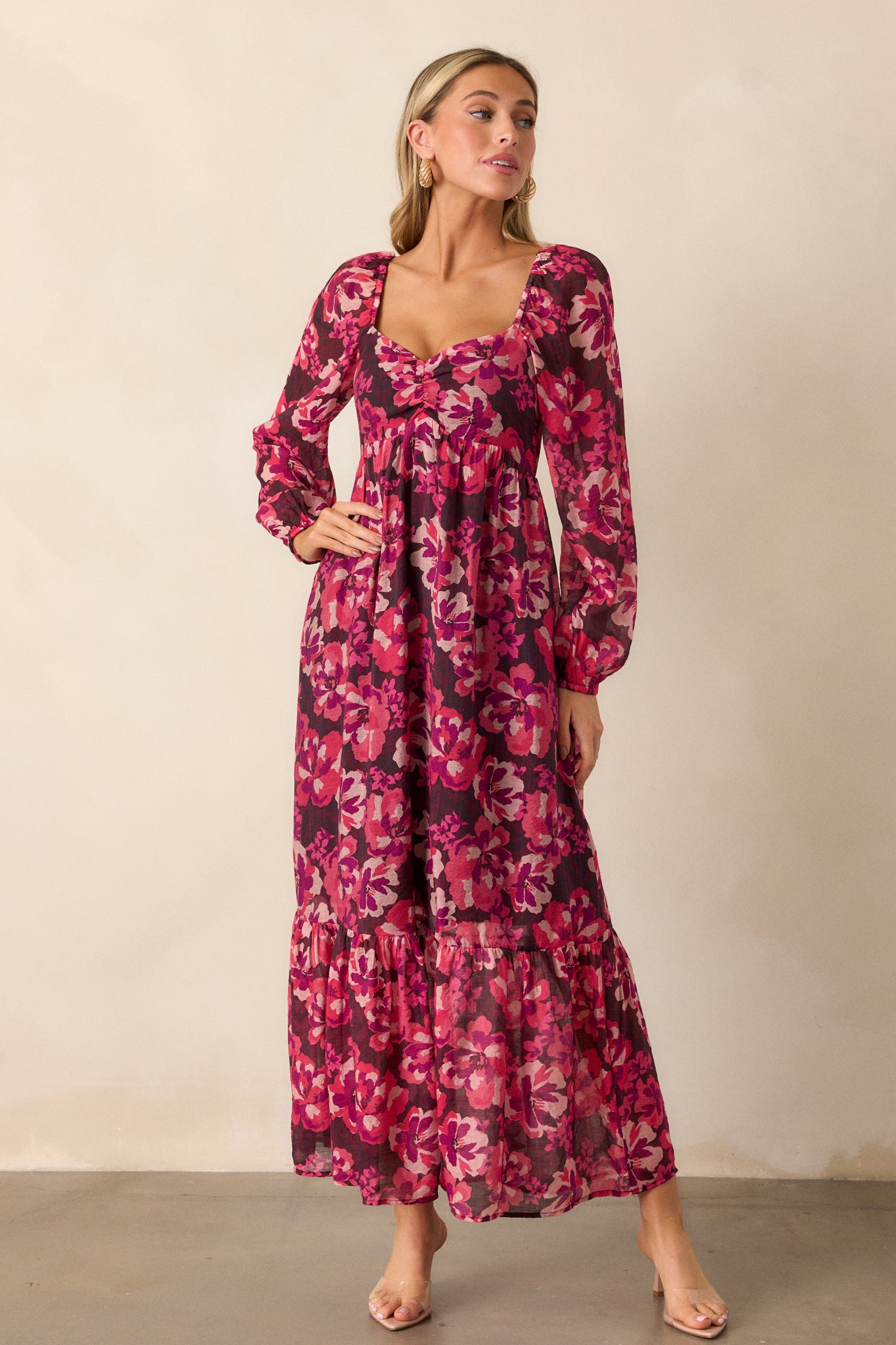 A pink dress featuring a slight v-neckline and a beautiful floral pattern, showcasing the flowing tiered skirt that falls to a midi length.