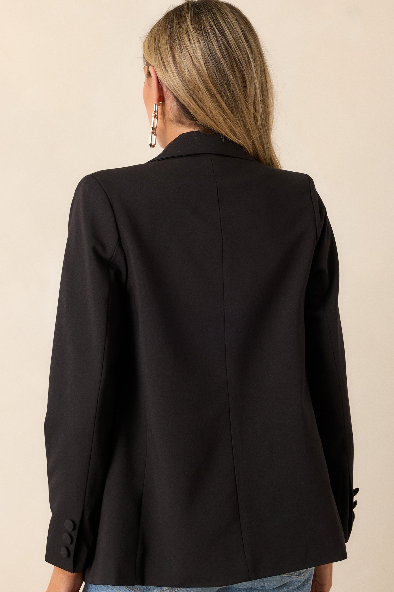 Back view of this black blazer that  features two functional pockets, functional buttons, a lapel collar, lightweight shoulder pads, and a multicolor print lining.