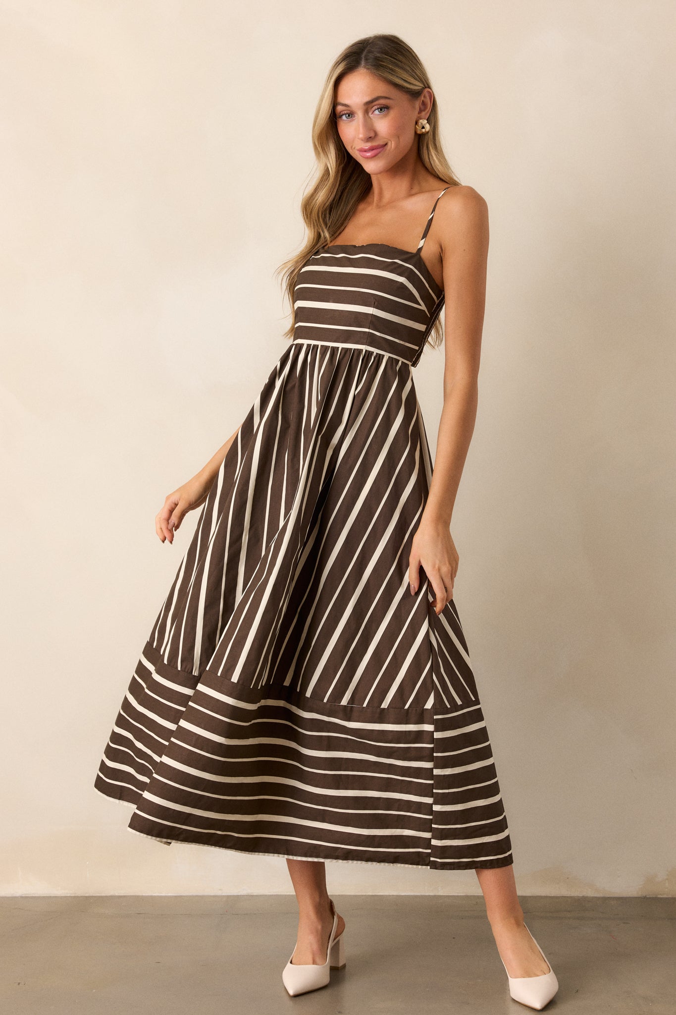 Angled view of the brown dress, highlighting the flowing midi length and the unique stripe patterns that alternate throughout the fabric.