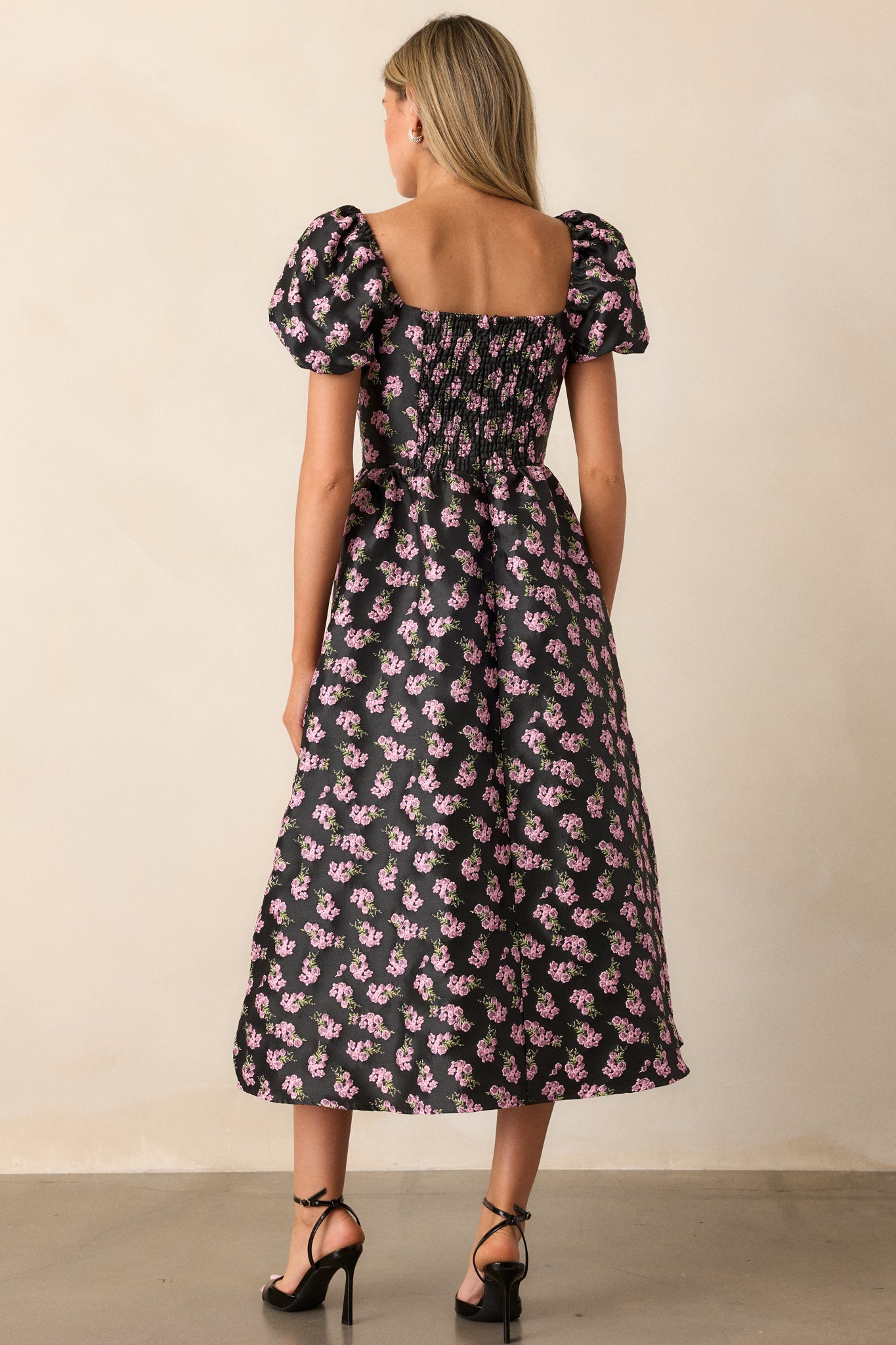 The back of the black midi dress featuring a smocked detail, highlighting the fitted bodice and puff sleeves while maintaining the stylish silhouette.