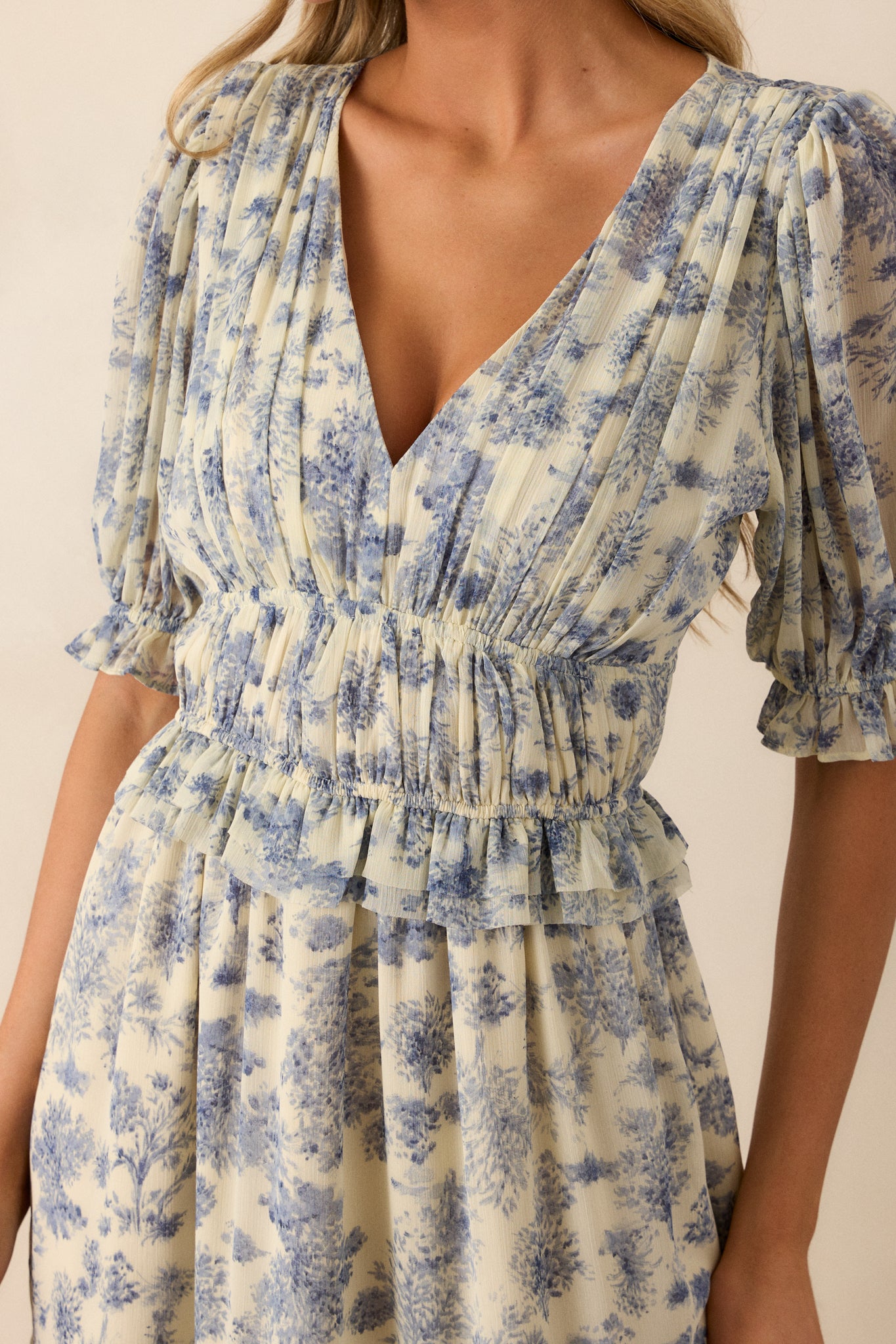 Extreme close-up of the blue floral pattern on the dress, highlighting the intricate design and the soft texture of the fabric along the v-neckline.