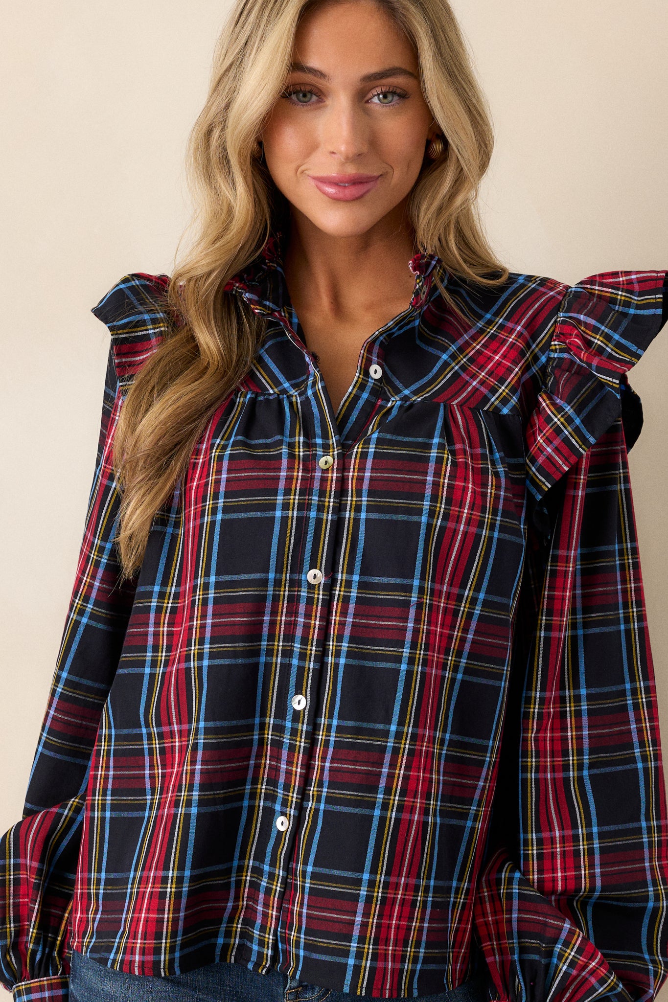 This black plaid top features a ruffle round neckline, ruffle sleeve detail, functional buttons down the center, wide sleeves, and buttoned cuffs. 